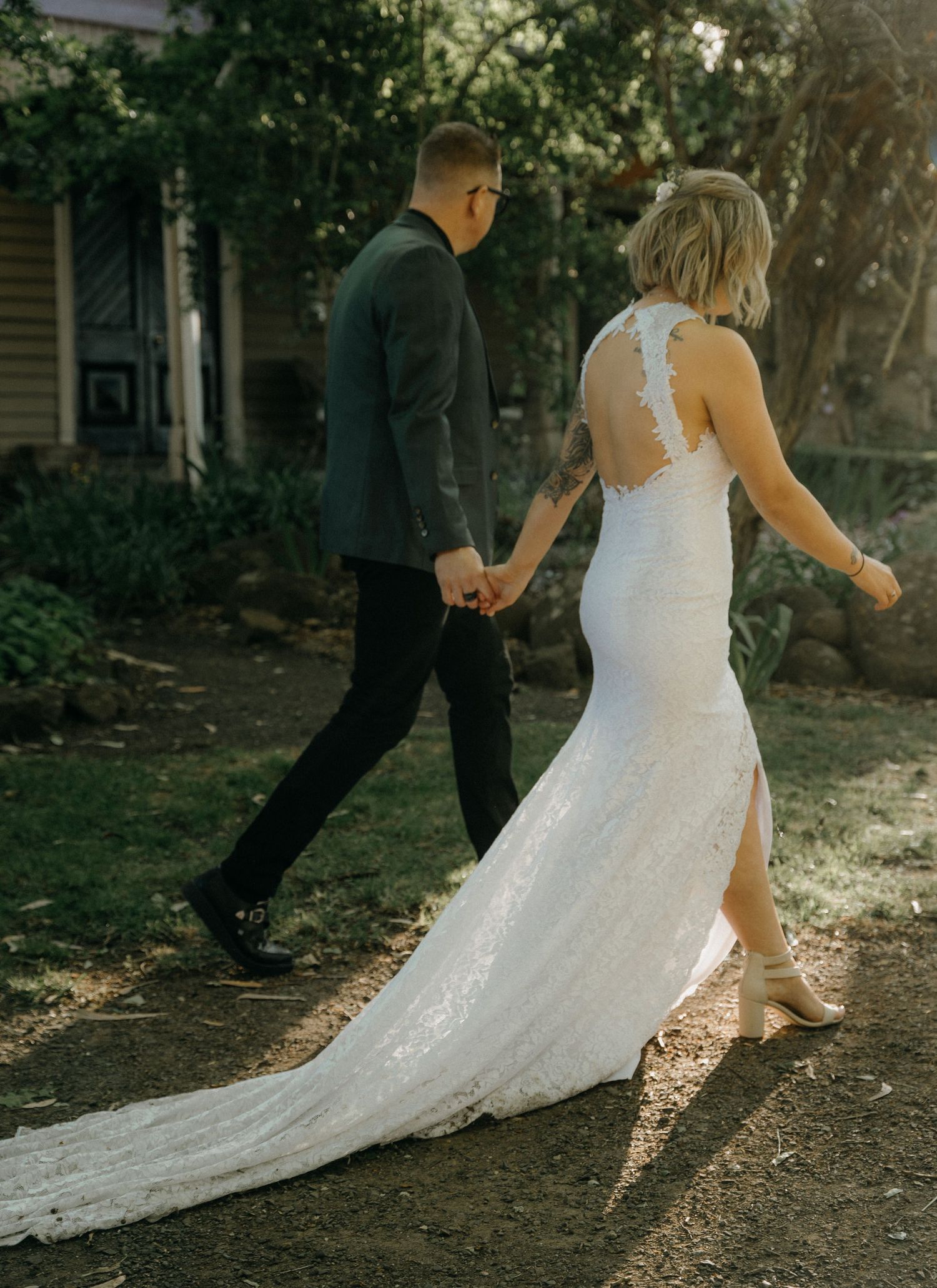 A couple walking together outdoors, with the bride wearing a stunning lace back wedding gown with a flowing train.