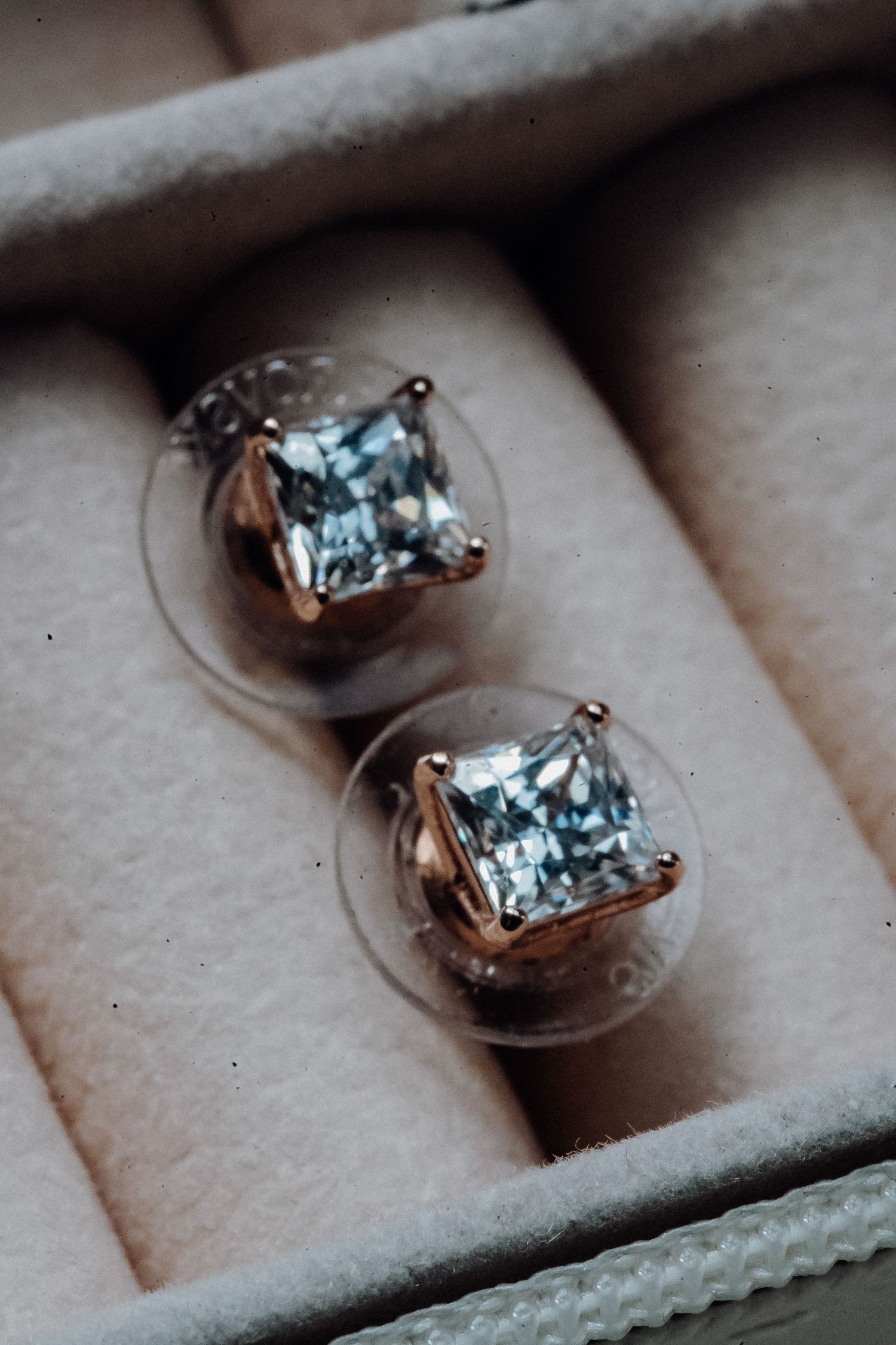 Close-up macro shot of sparkling diamond earrings in rose gold settings displayed in a beige jewelry box.