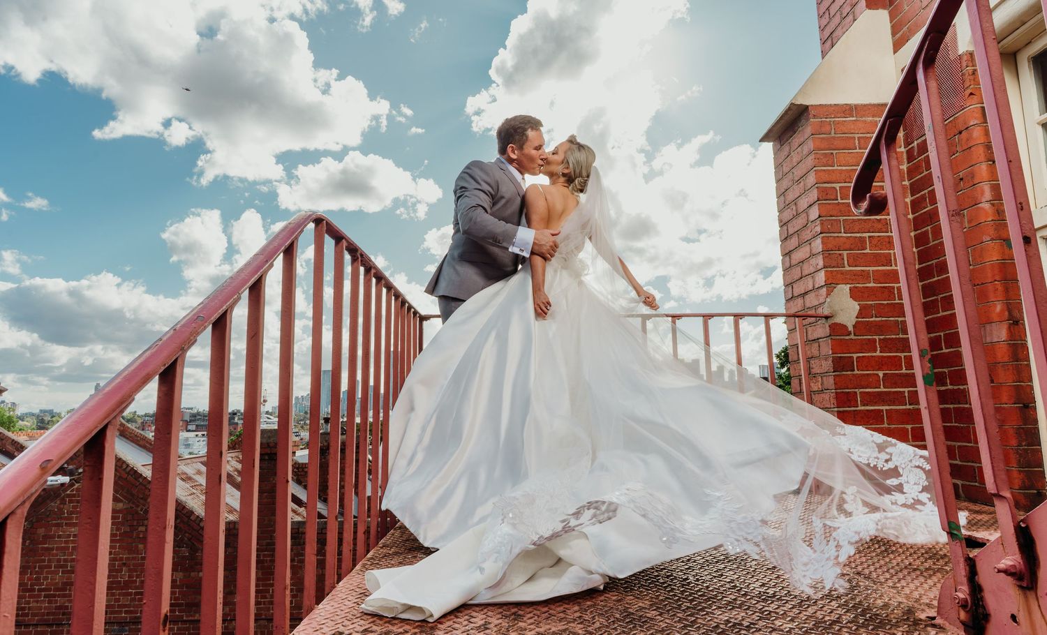 A couple in wedding attire shares romantic moments on a rustic wooden deck with mountains in the background.