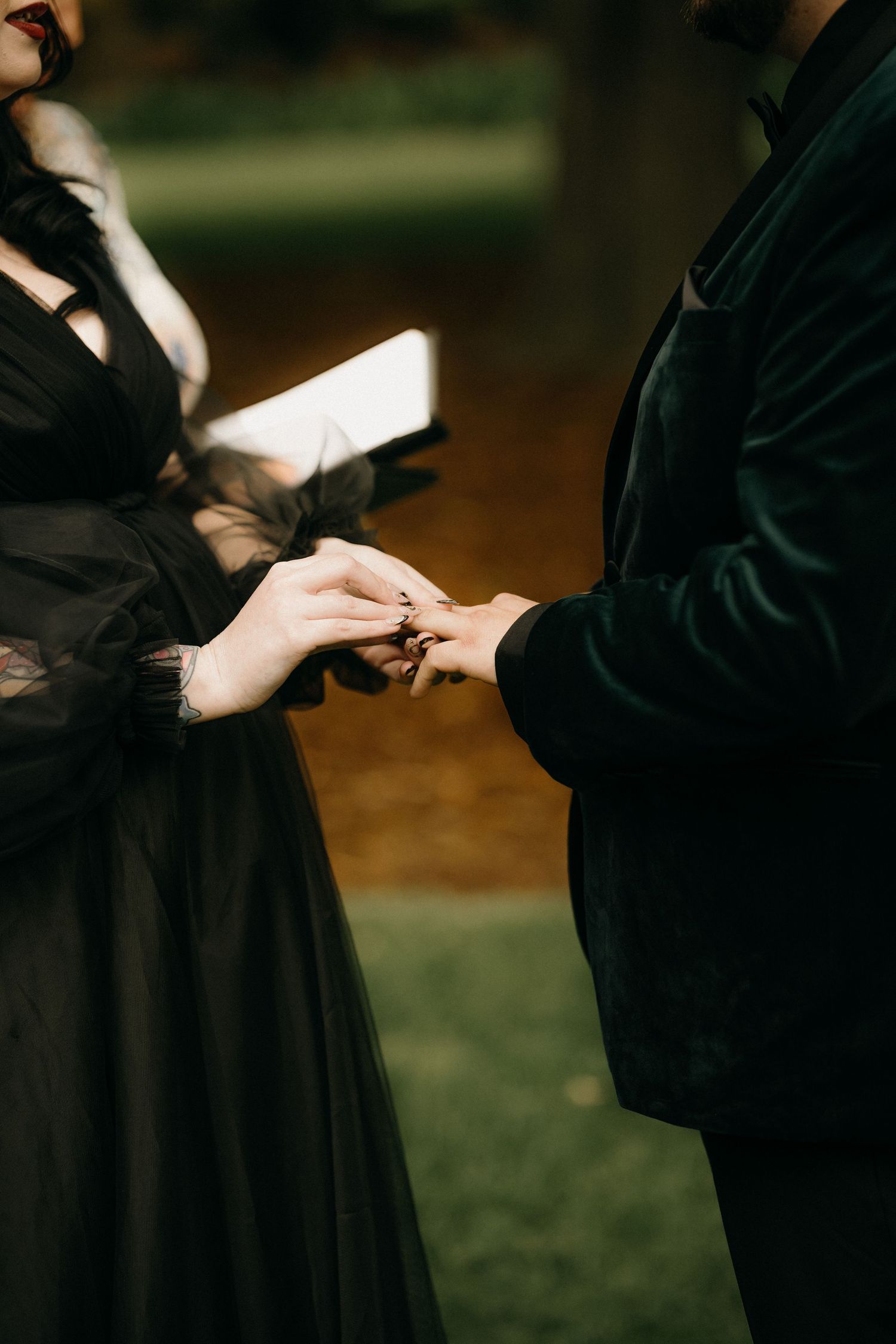 Two people in black graduation gowns exchange diplomas during a graduation ceremony outdoors.
