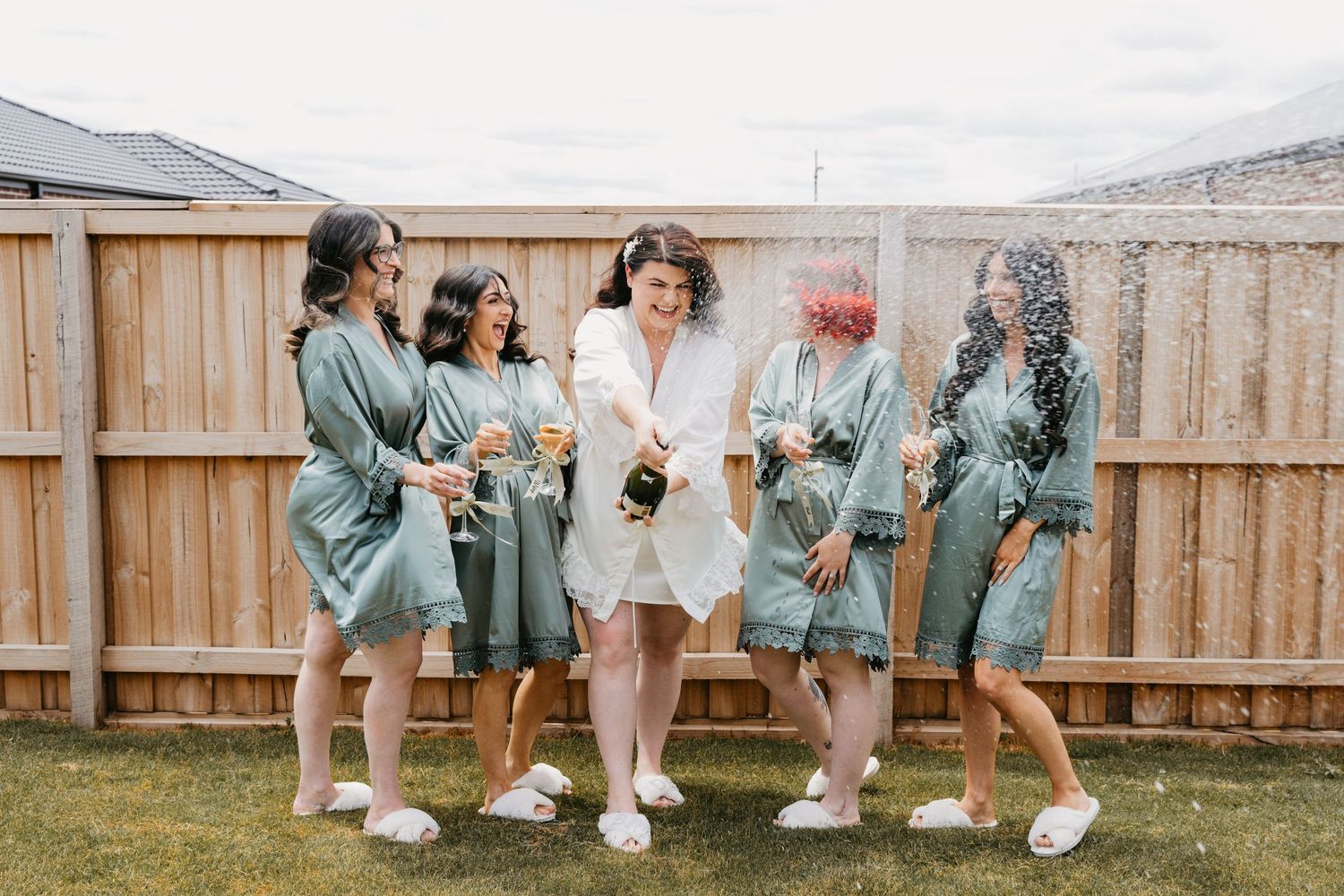 A row of bridesmaids in sage green dresses show off their white sneakers in a candid backyard photo.