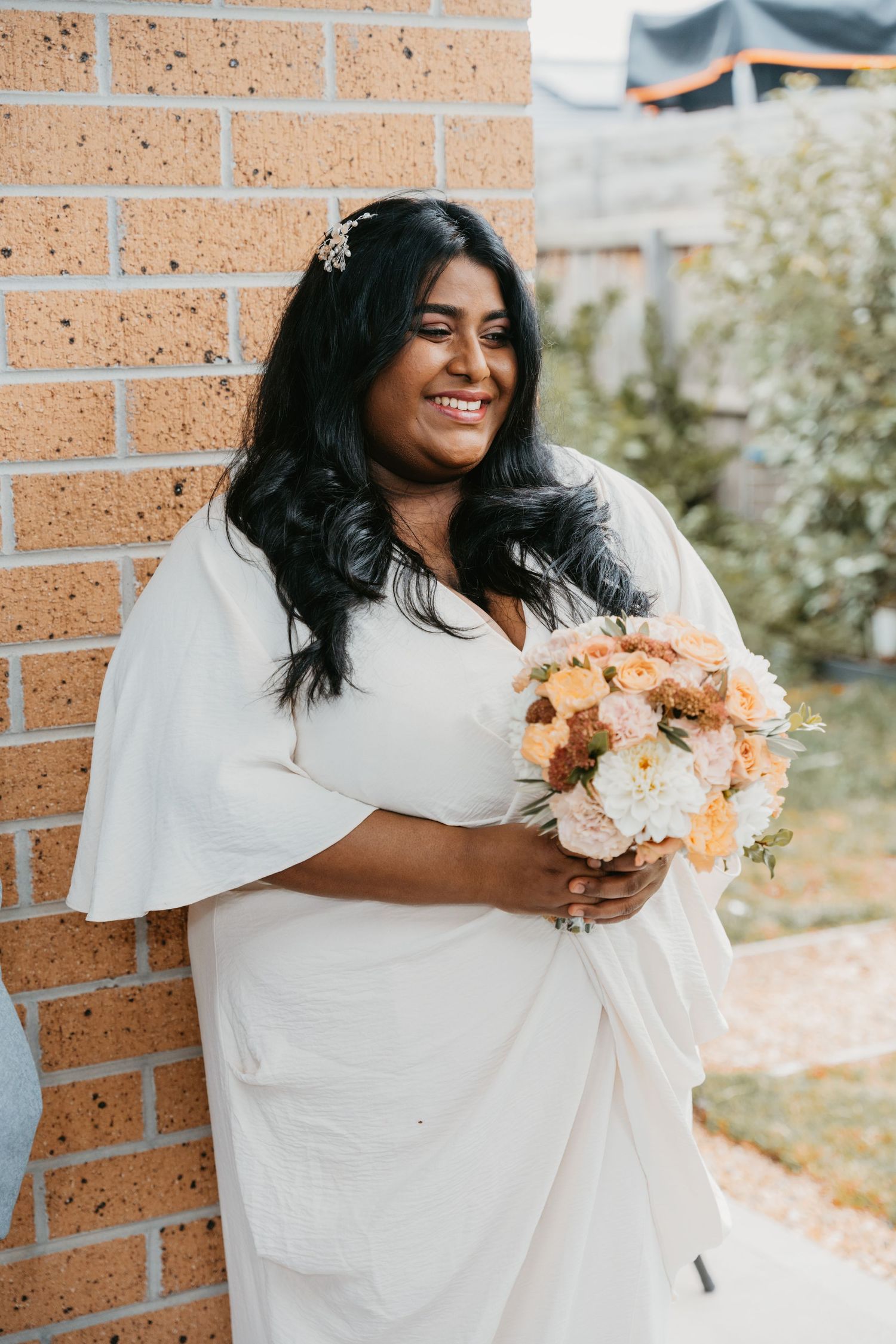 Multiple frame shots of someone in a white wedding dress holding a beautiful peach and cream bouquet against a brick wall.