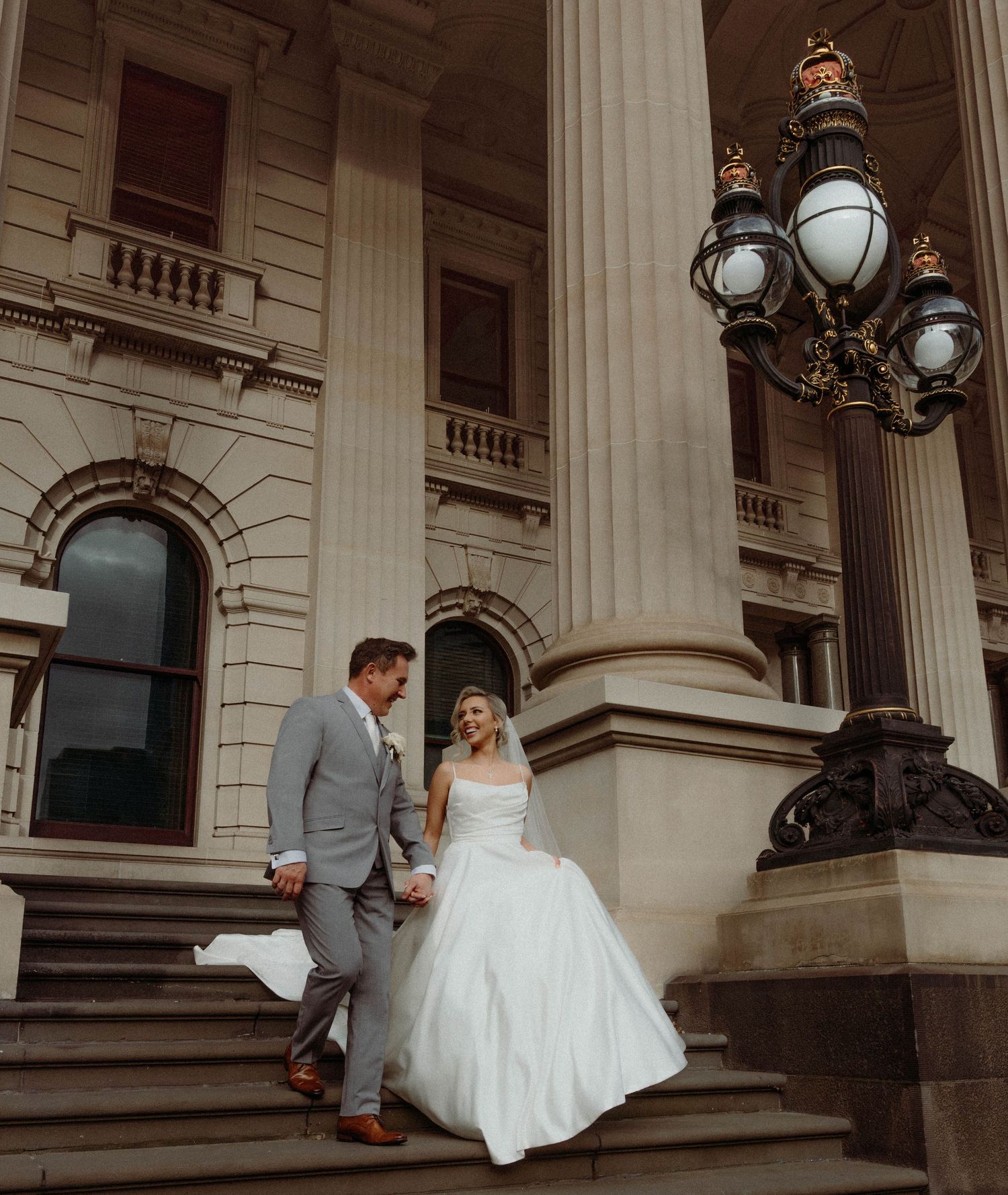 A couple in wedding attire sitting on grand stone steps of a historic building with classical columns.