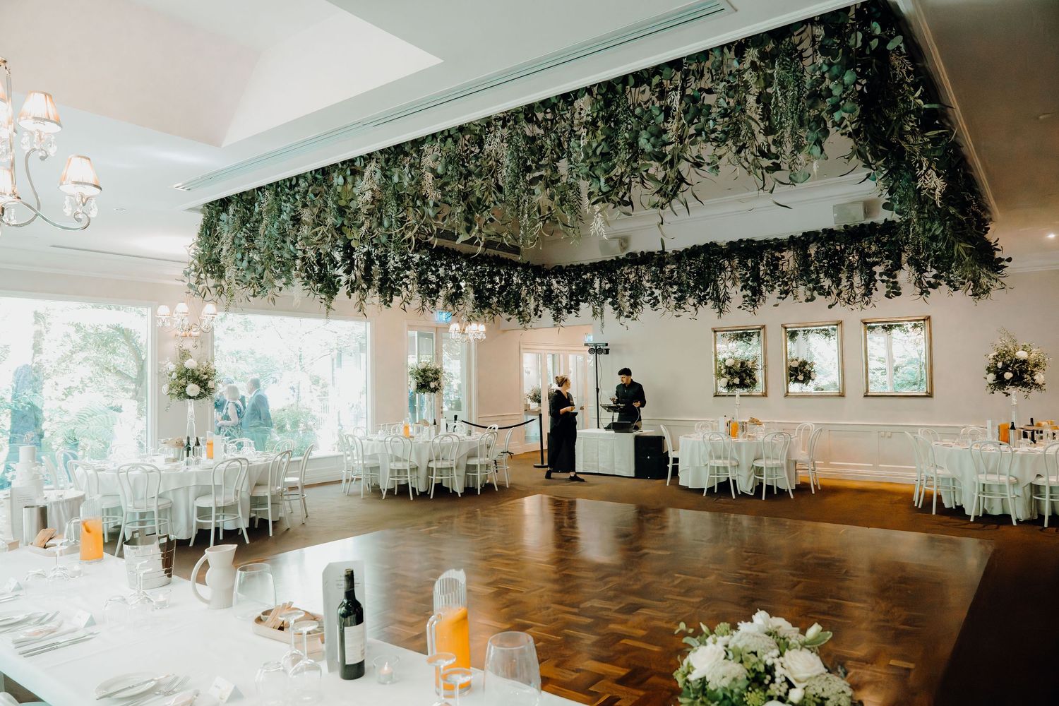 Elegant wedding reception venue with hanging greenery decor and soft lighting illuminating the dance floor.