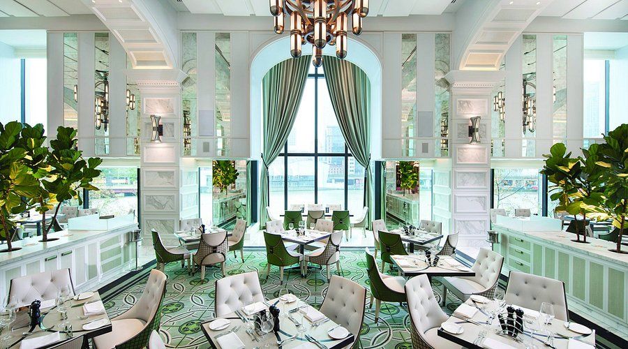 Elegant dining room with mint green decor, white columns, crystal chandelier and floor-to-ceiling windows overlooking the ocean.