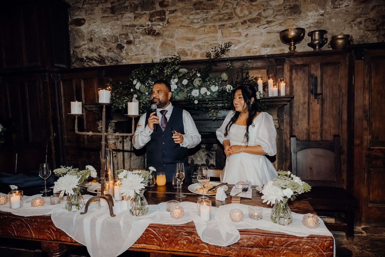 A rustic barn wedding reception with orange and white floral decor, vintage furniture, and warm candlelight.