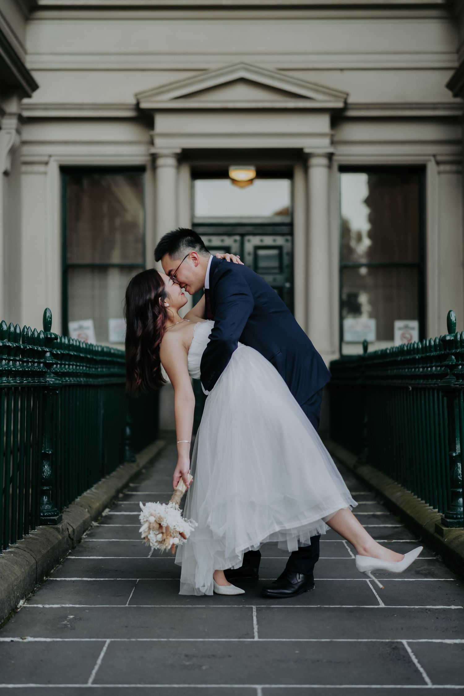 A couple in wedding attire shares a romantic moment on a stone patio with black iron railings in a sequence of photos.