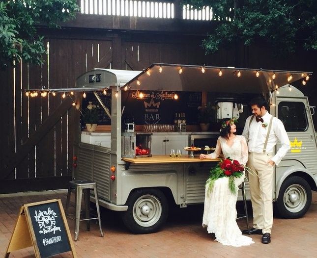 A vintage white food truck parked at an outdoor event with string lights and wooden fencing in the background.