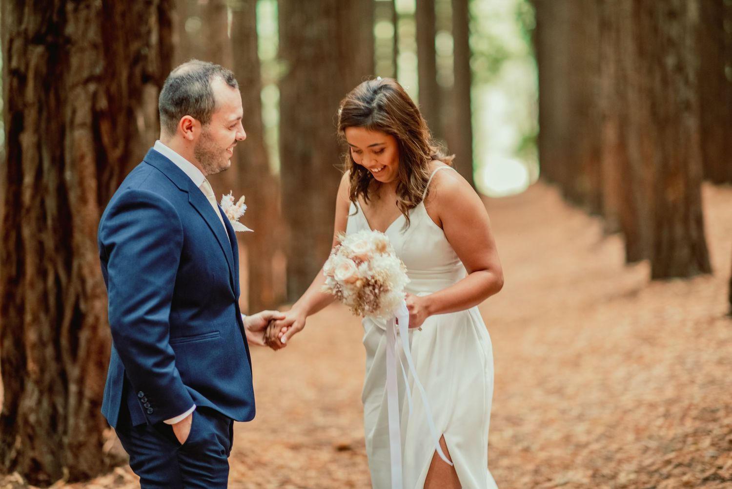 Couple shares romantic moment in redwood forest with bride in white dress and groom in navy suit.