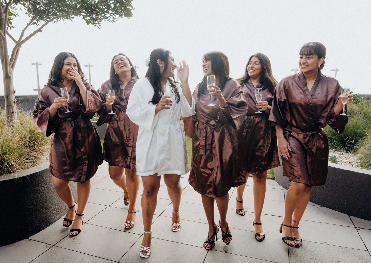 A group of friends in matching silk robes walk together while holding drinks during a celebration event.