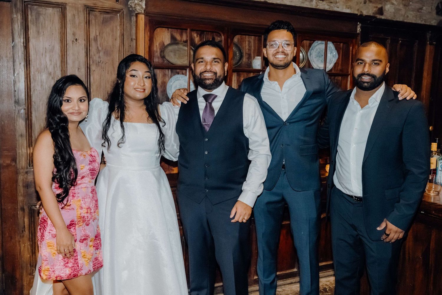 A wedding party poses together in a rustic wooden venue with formal attire.