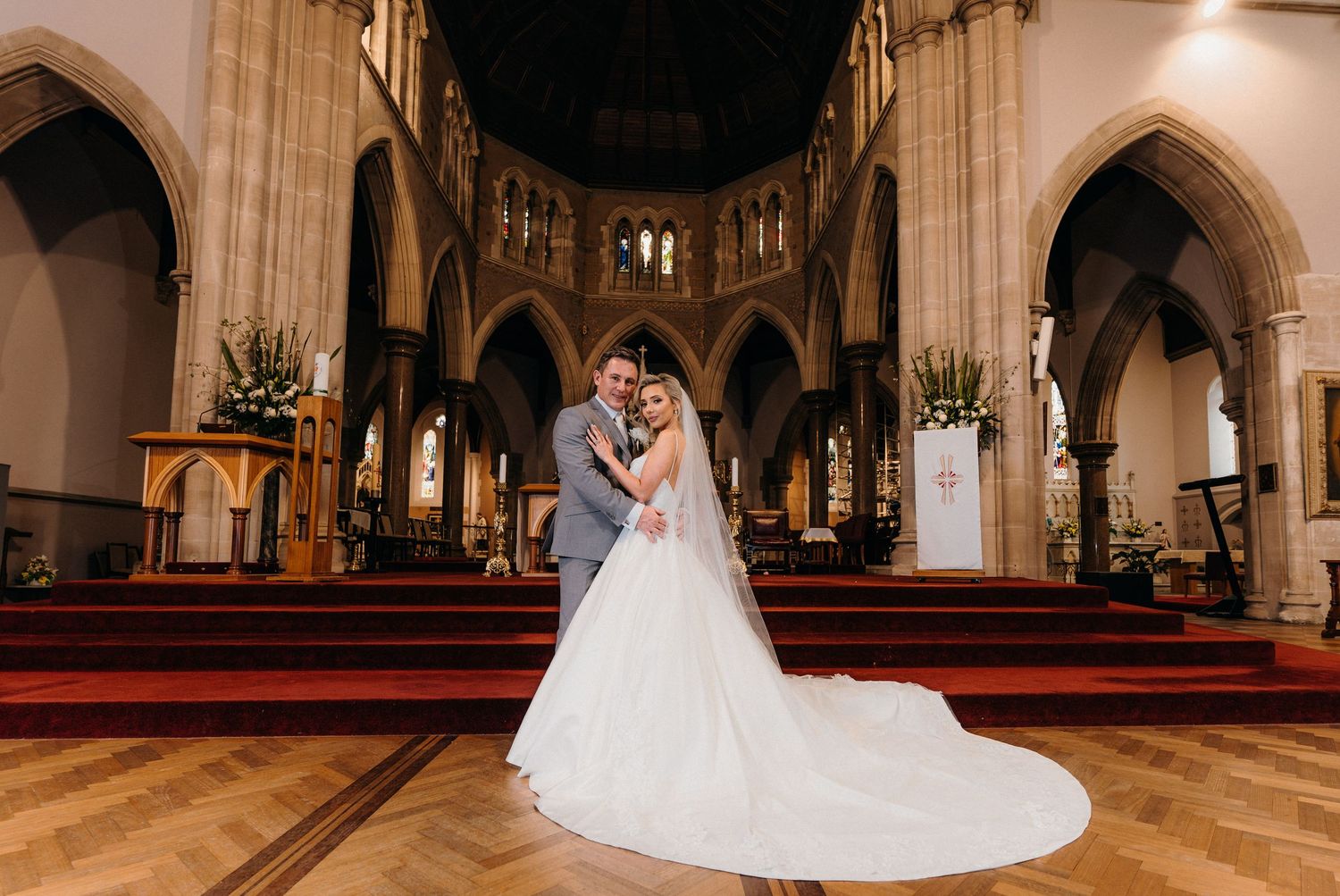 A couple embraces in a beautiful Gothic church interior with vaulted arches and ornate architectural details.