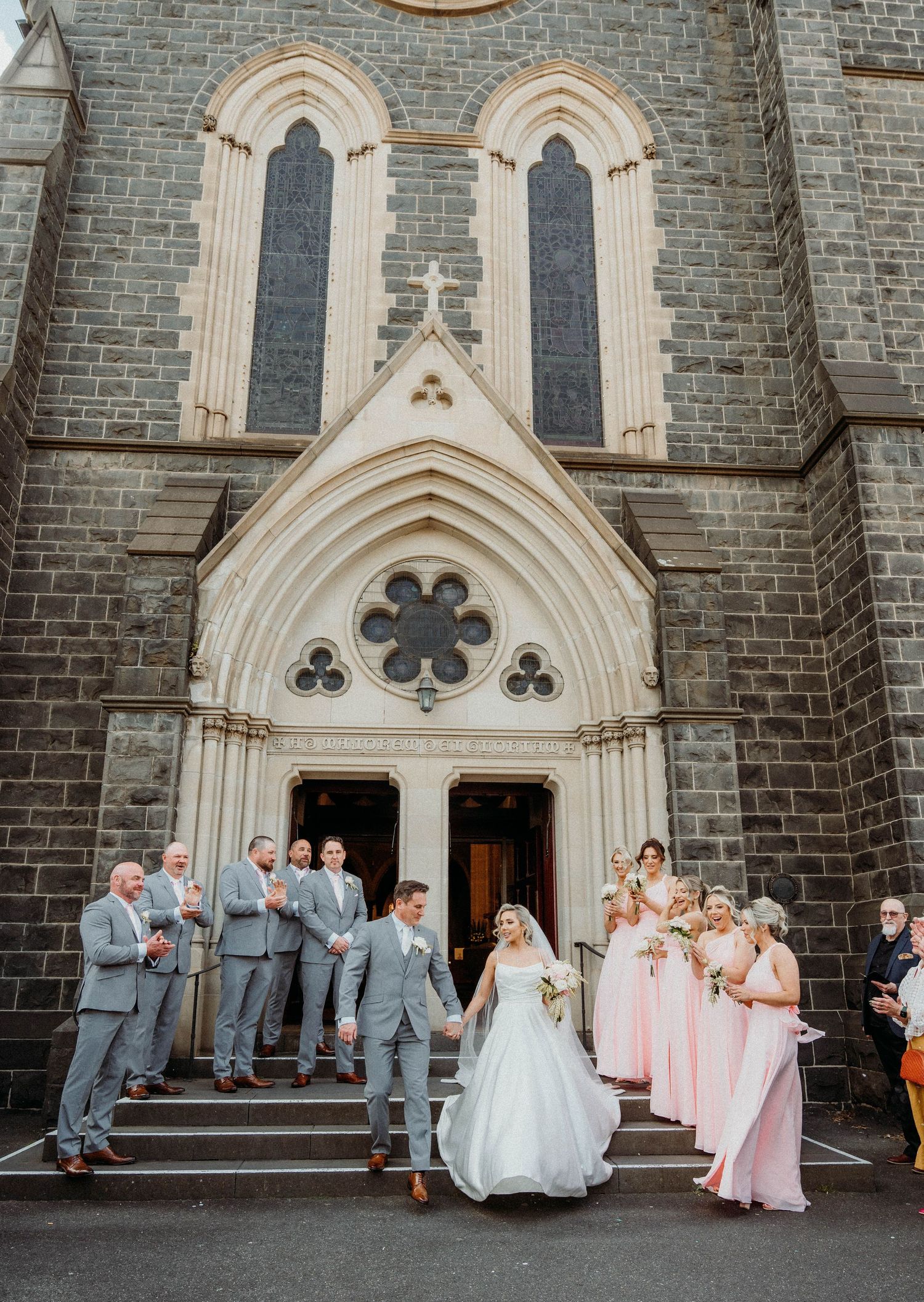 Wedding party members gather outside a gothic stone church with arched doorways and decorative architecture.