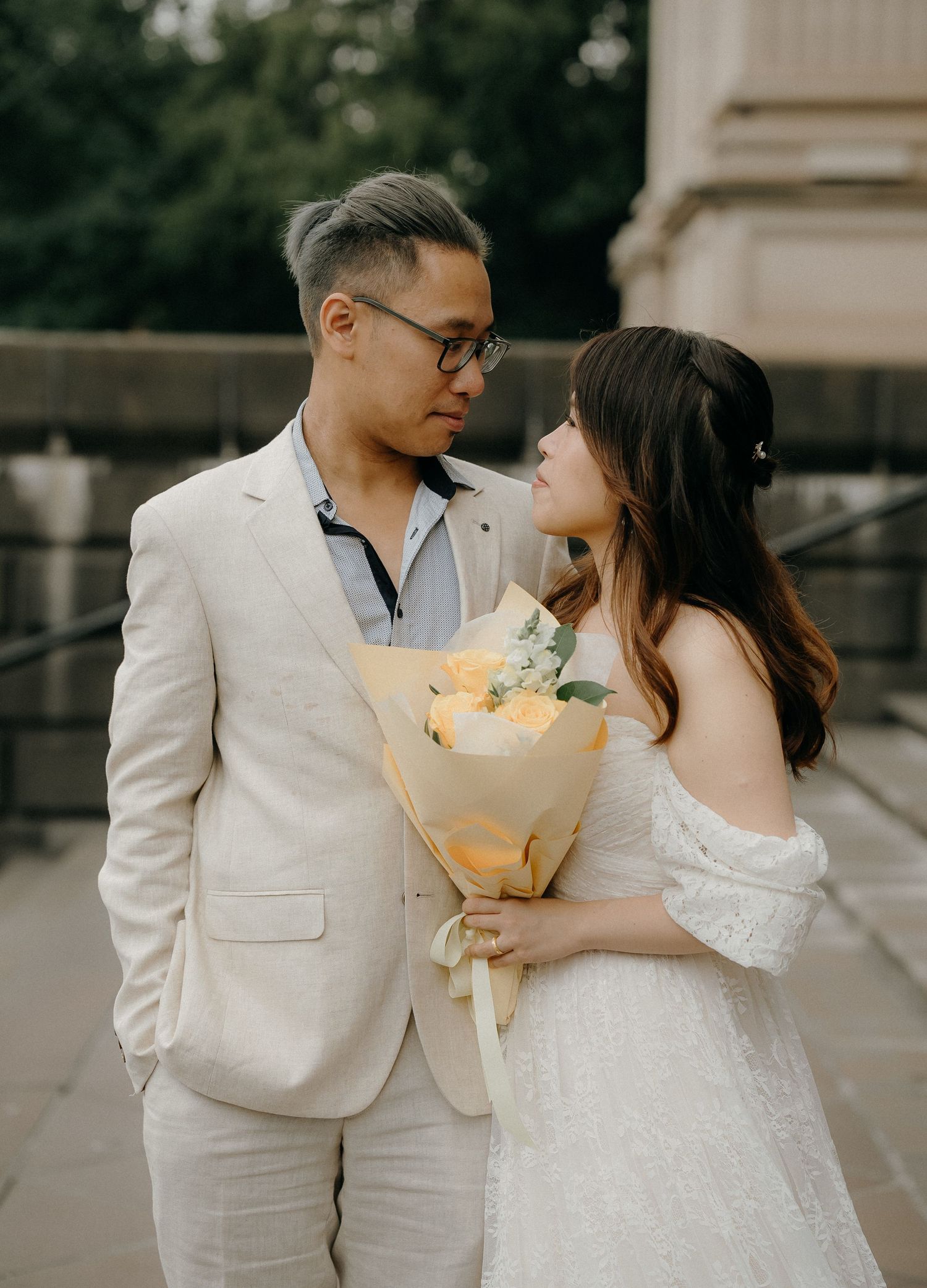 Romantic couple in white attire share tender moments while holding a glowing bouquet during an evening photoshoot.