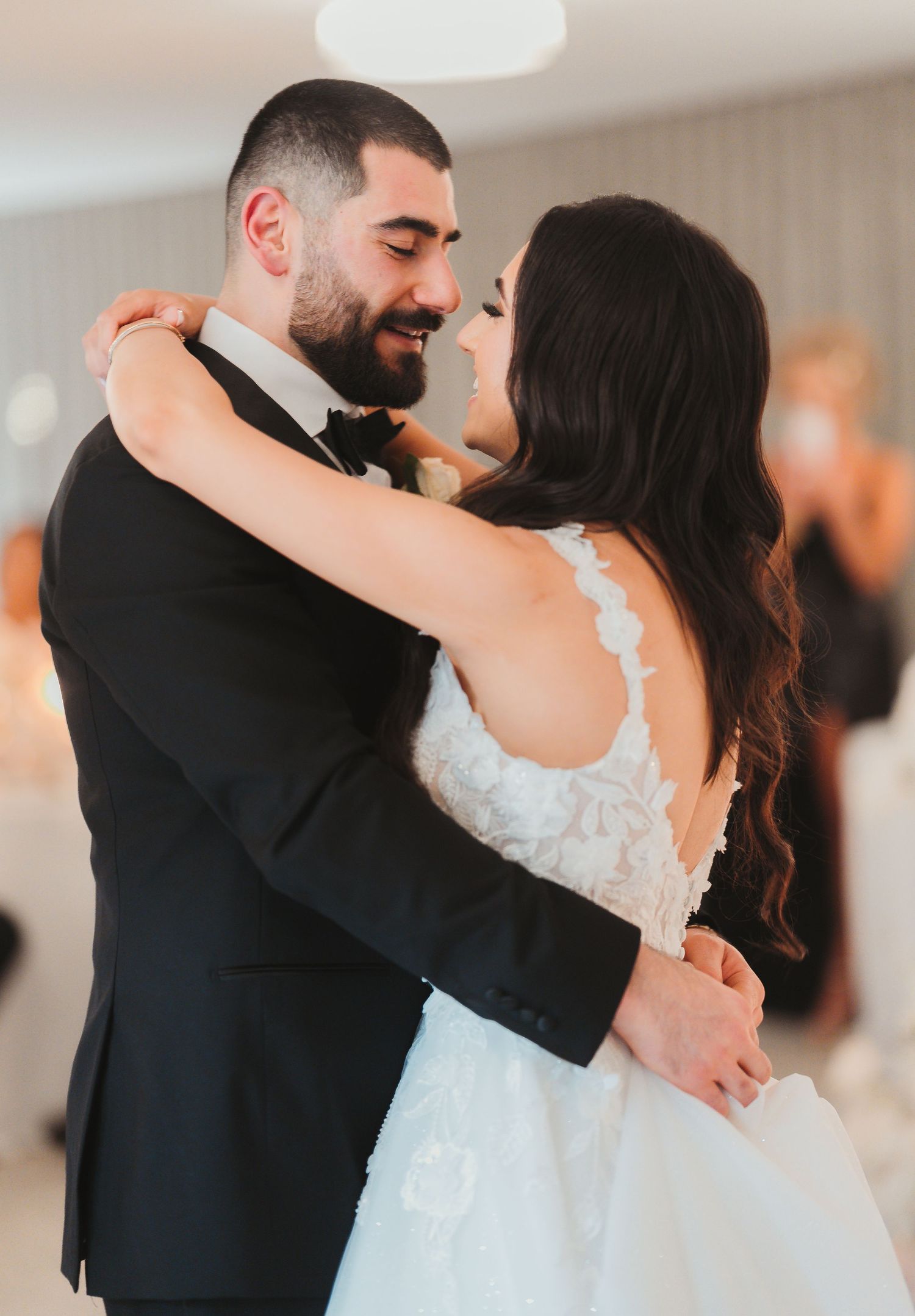 A couple shares an intimate moment during their first dance at their wedding celebration, dressed in formal attire.
