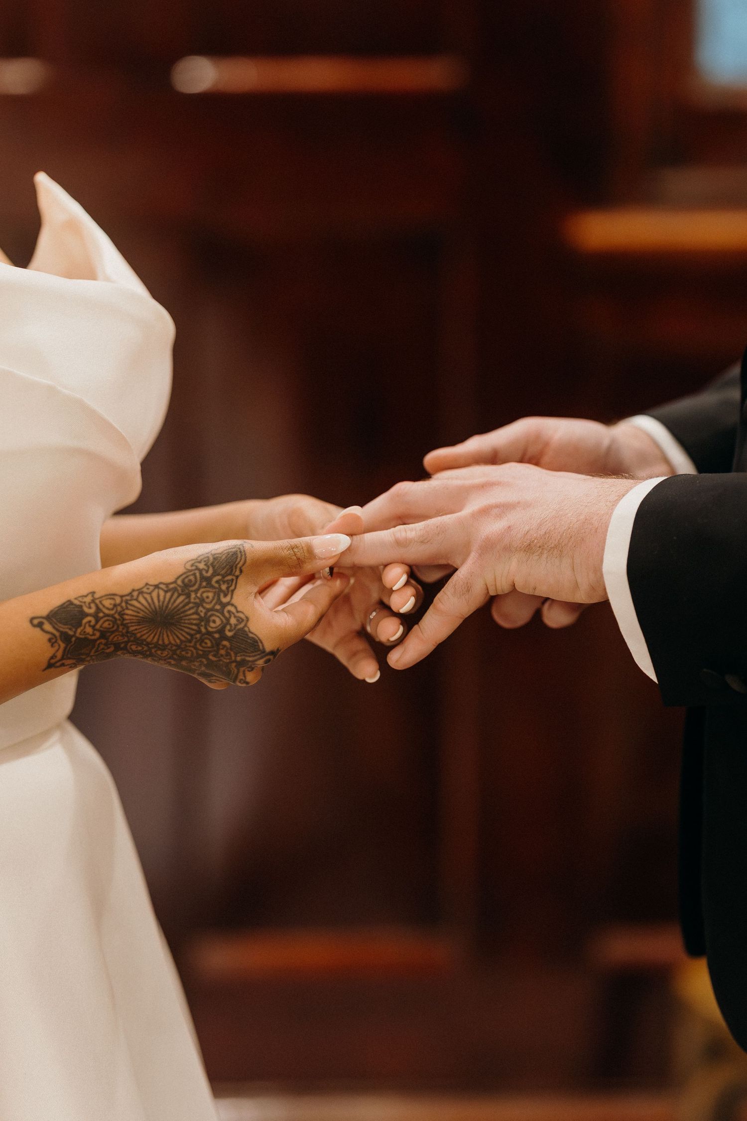 Bride with henna tattoo placing wedding ring on groom's finger during ceremony.