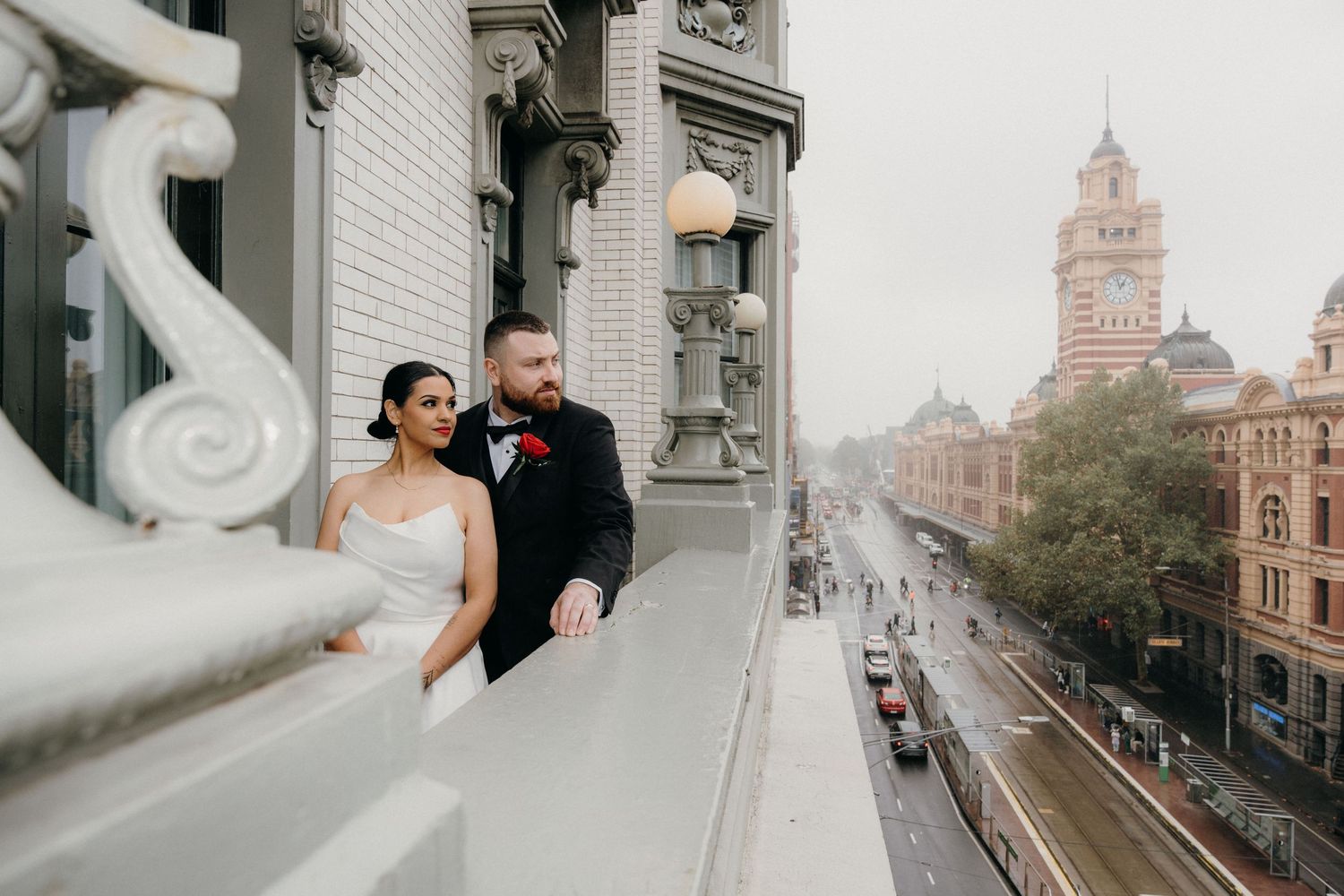 Bride and groom stand on a grand balcony overlooking Melbourne's Flinders Street Station on their wedding day.