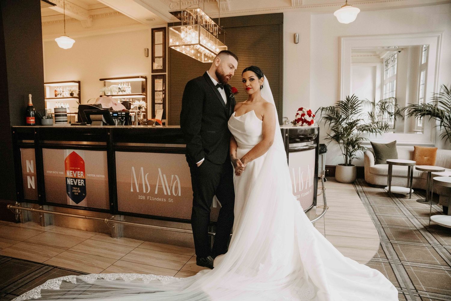 Elegant bride and groom posing together in a luxurious hotel lobby near a stylish bar on their wedding day.