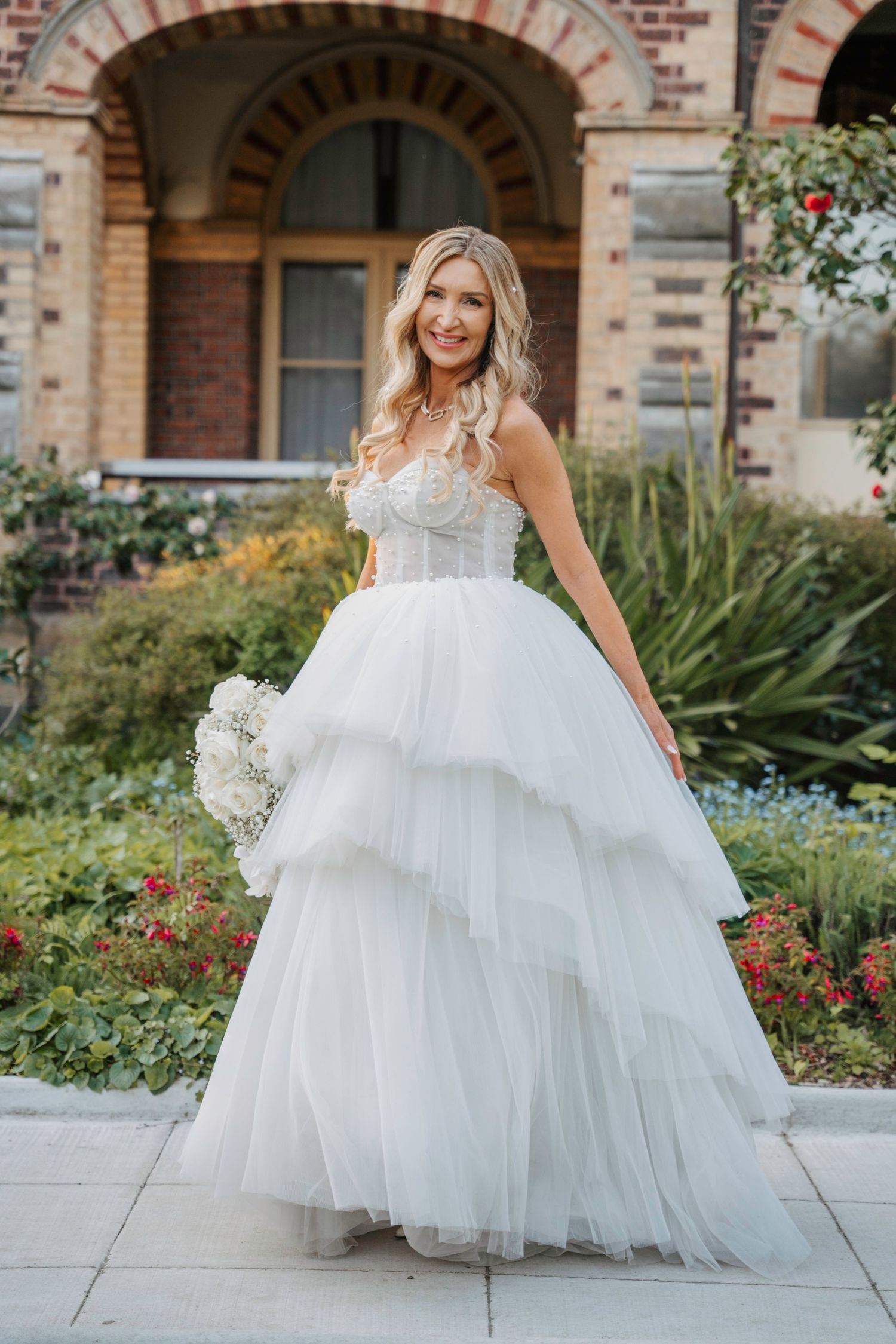 Beautiful wedding dress with tiered tulle skirt and structured corset bodice in garden setting with brick architecture.