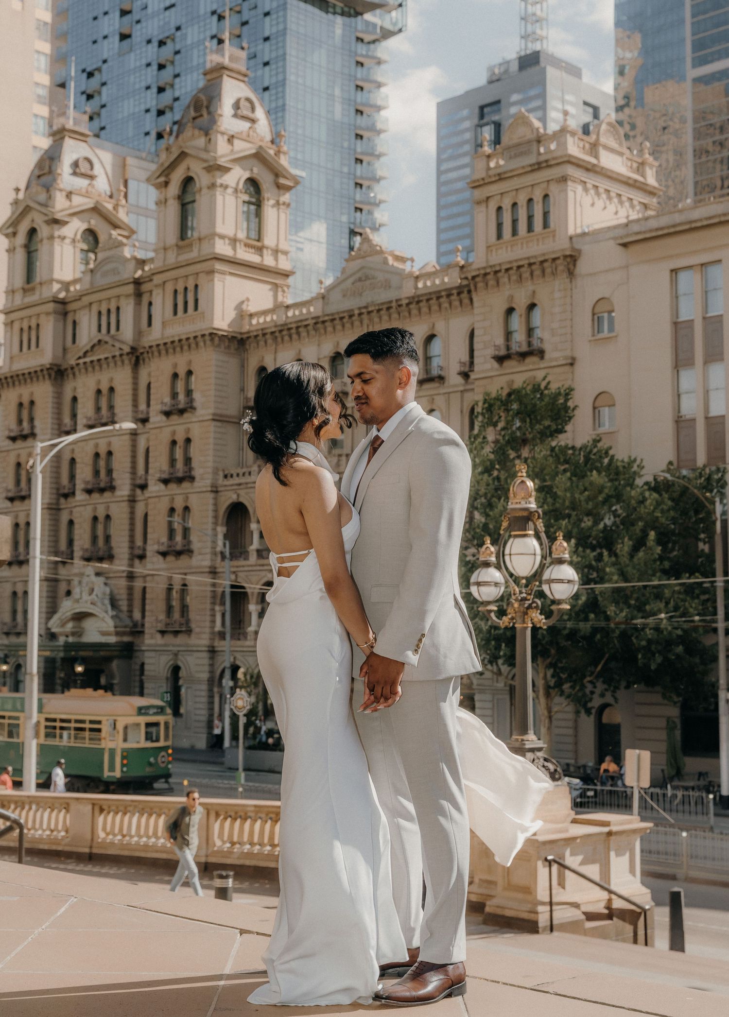 A couple in wedding attire share an intimate moment in front of an ornate historic building with grand architecture.