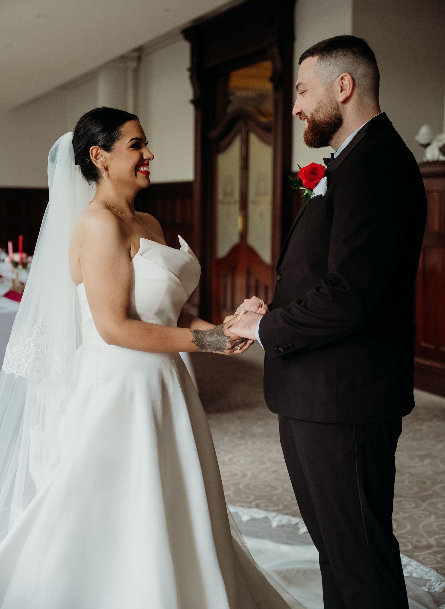 Bride in white gown and veil holds hands with groom in black suit during wedding ceremony.
