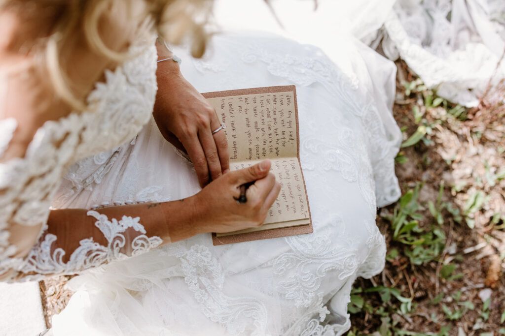 Someone in a white lace dress holds an open vintage book while sitting outdoors among scattered leaves.