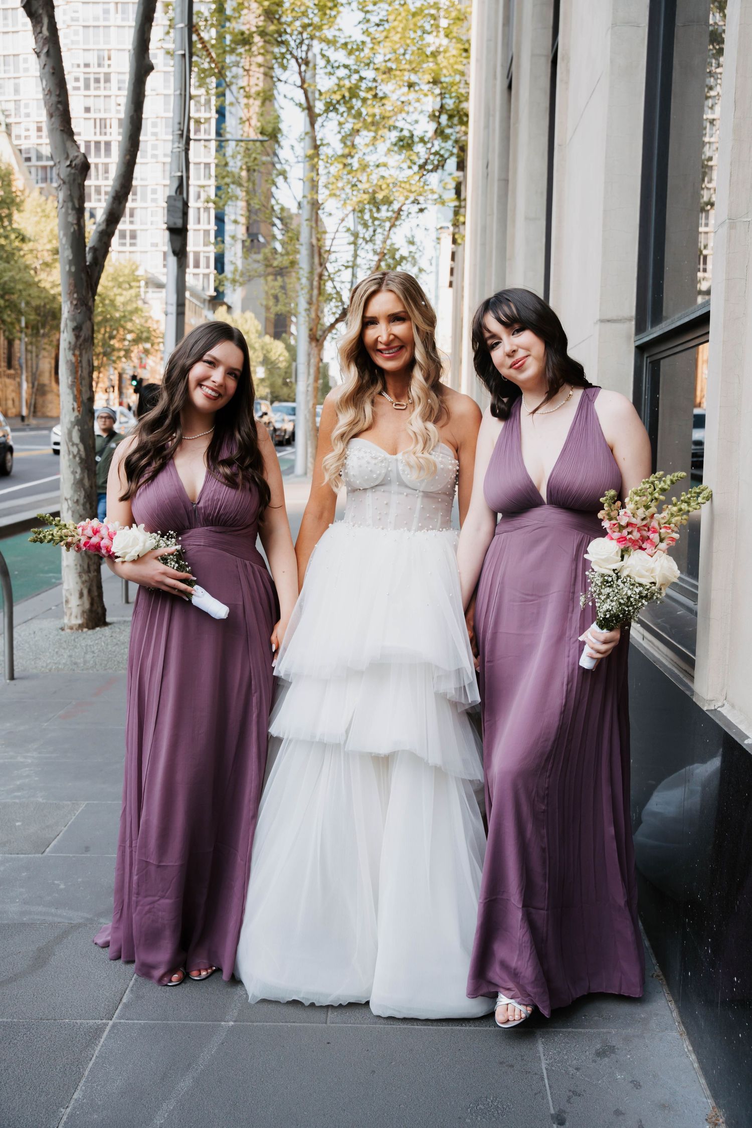 Wedding party poses together in purple bridesmaid dresses and white bridal gown on stone patio.
