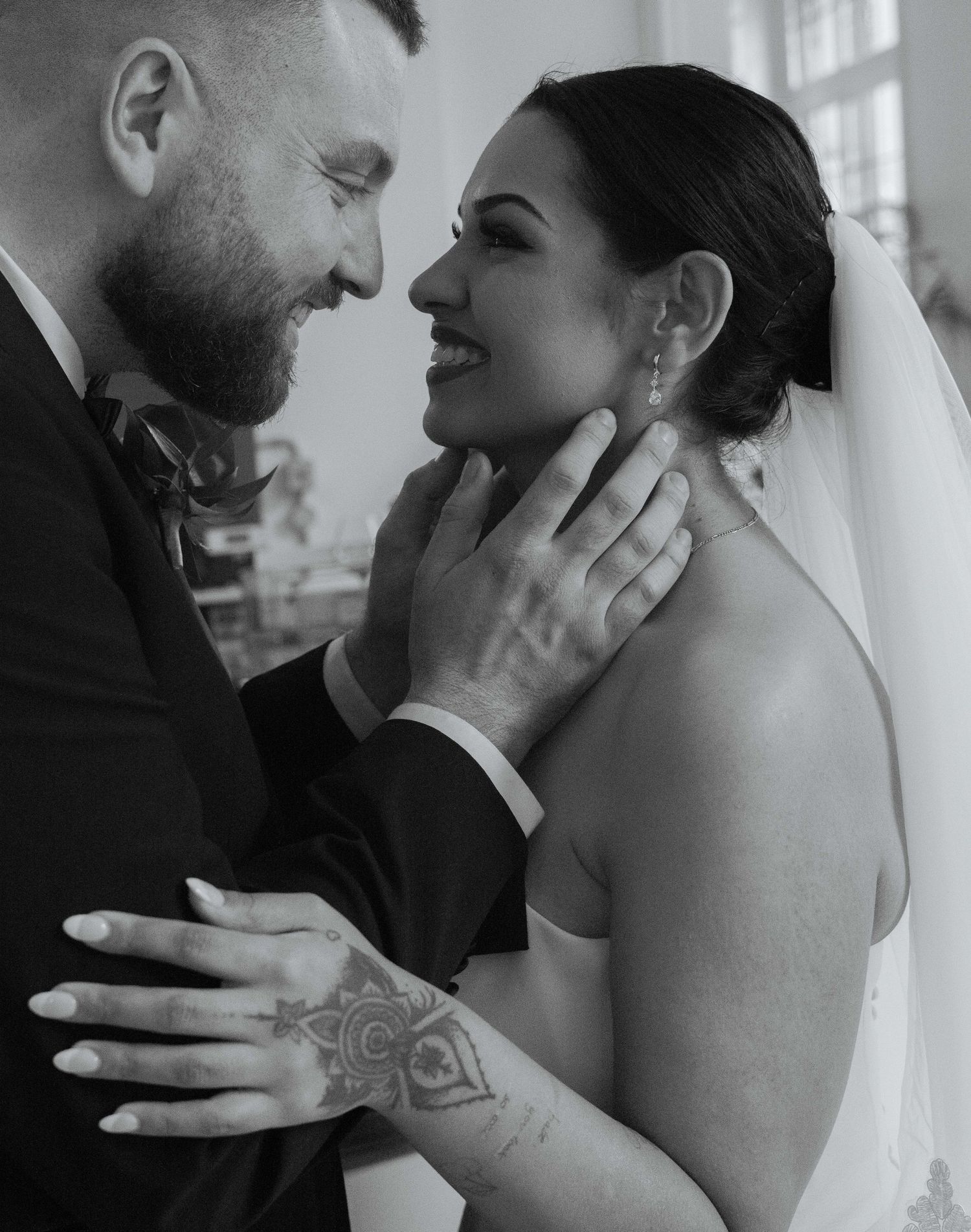 Black and white wedding photo of bride and groom sharing an intimate moment, groom cradling brides face, bride wearing veil.