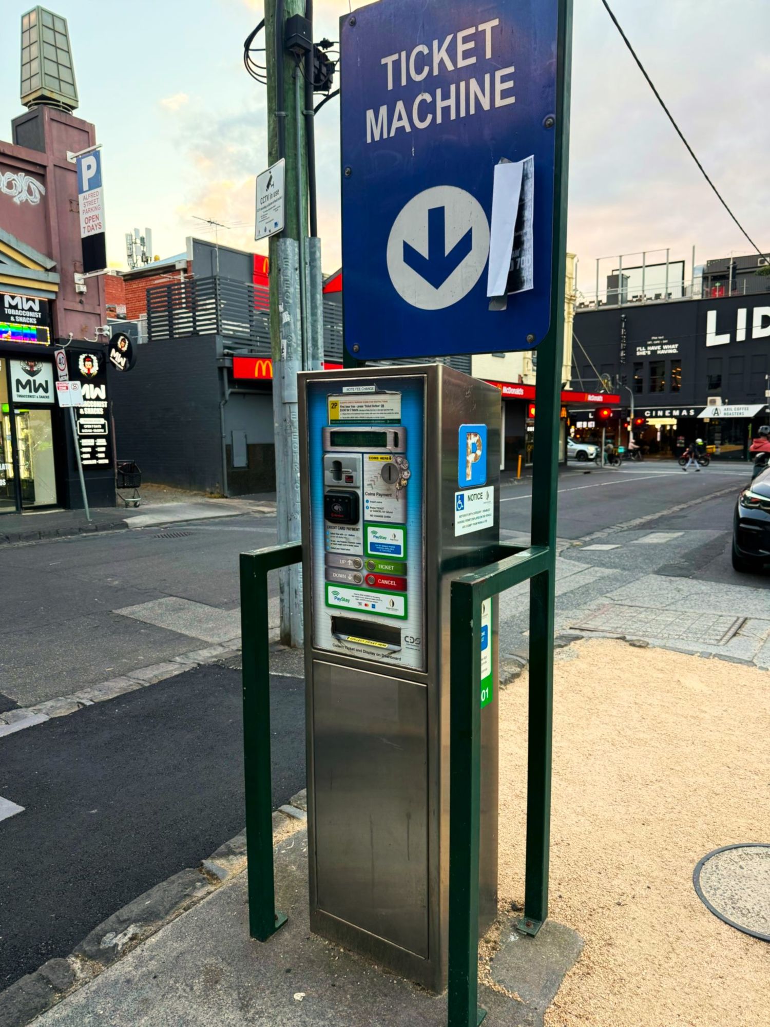 A series of parking ticket payment machines and kiosks on a city street with buildings in the background.