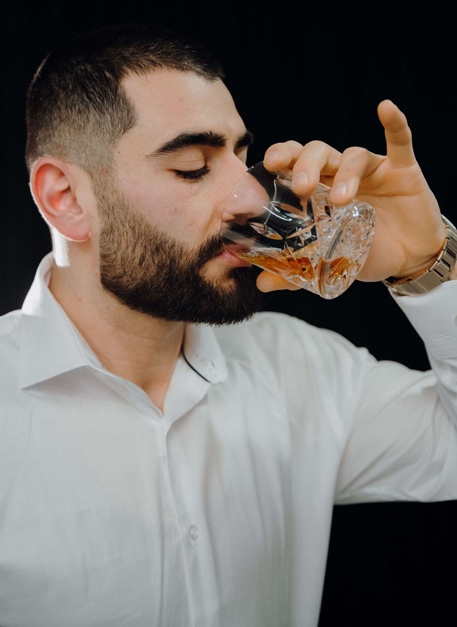 Person in white shirt taking shots of alcohol against black background in dramatic sequence.