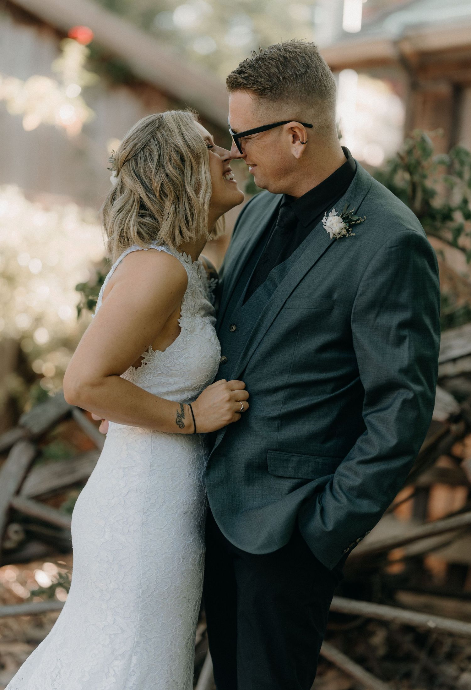 A couple in wedding attire share an intimate moment in a wooded setting with soft lighting and romantic atmosphere.