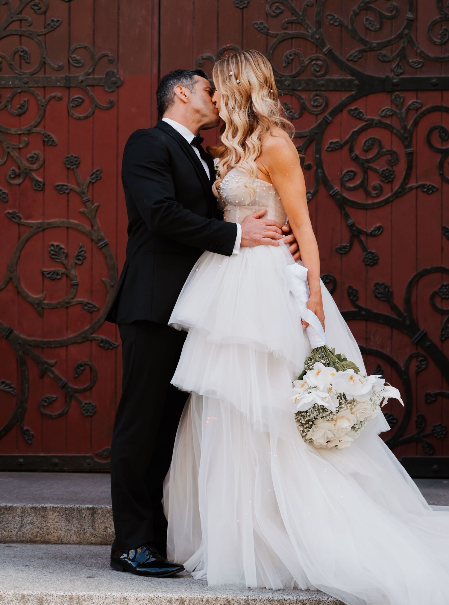 A romantic wedding couple embraces against an ornate red door in an artistic photo series.