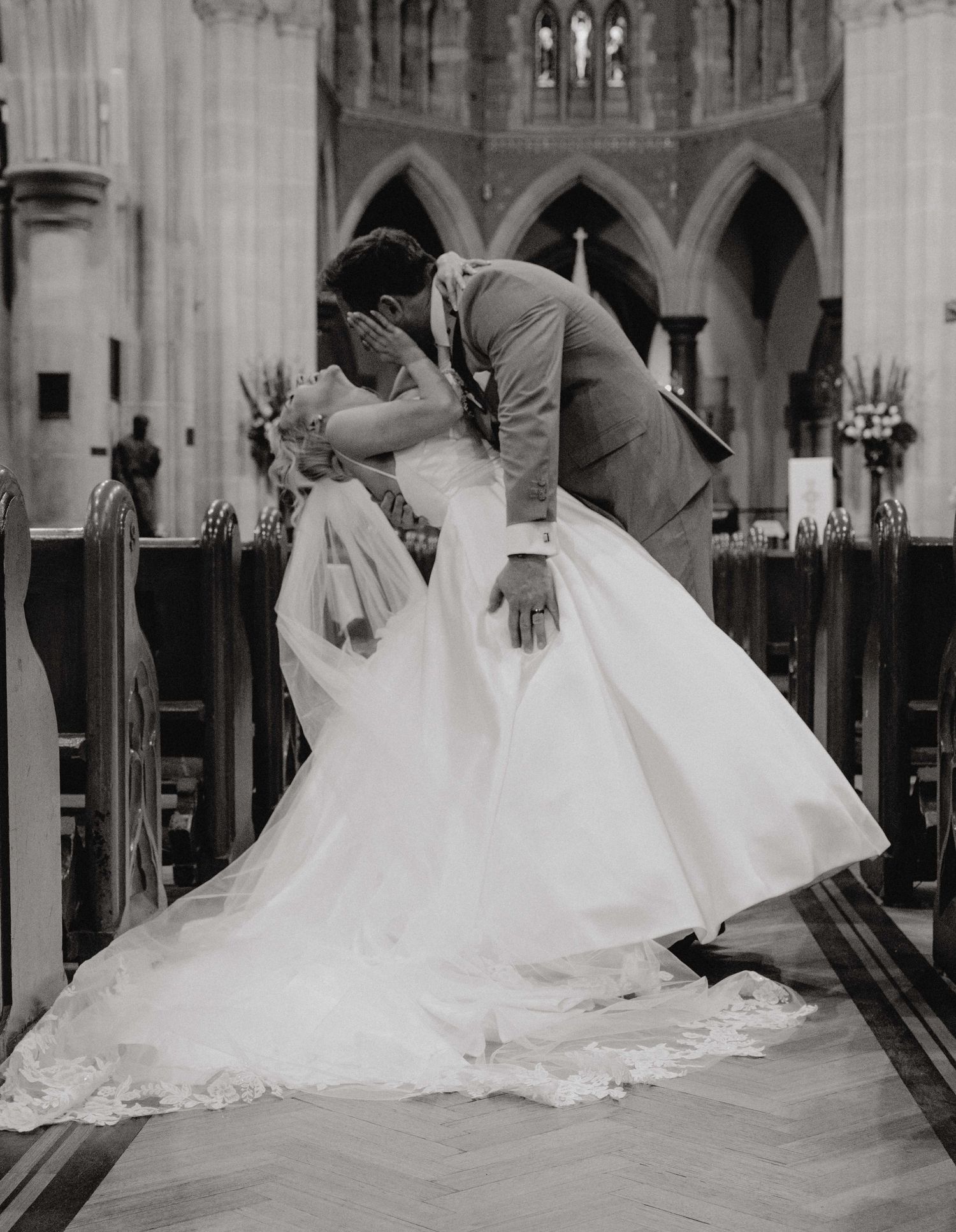 A series of wedding dresses with flowing trains displayed in a black and white photograph inside an elegant church.