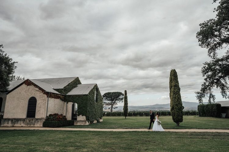 A panoramic view of a rustic farmhouse and barn buildings under dramatic cloudy skies in the countryside.