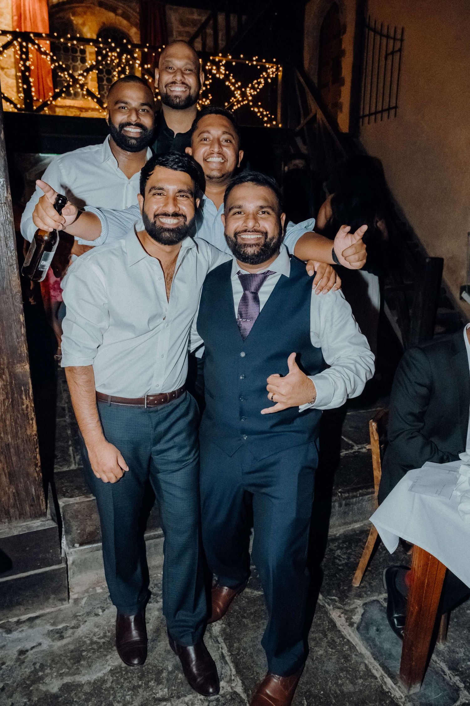 A group of friends smile together at a party with festive string lights decorating the background.