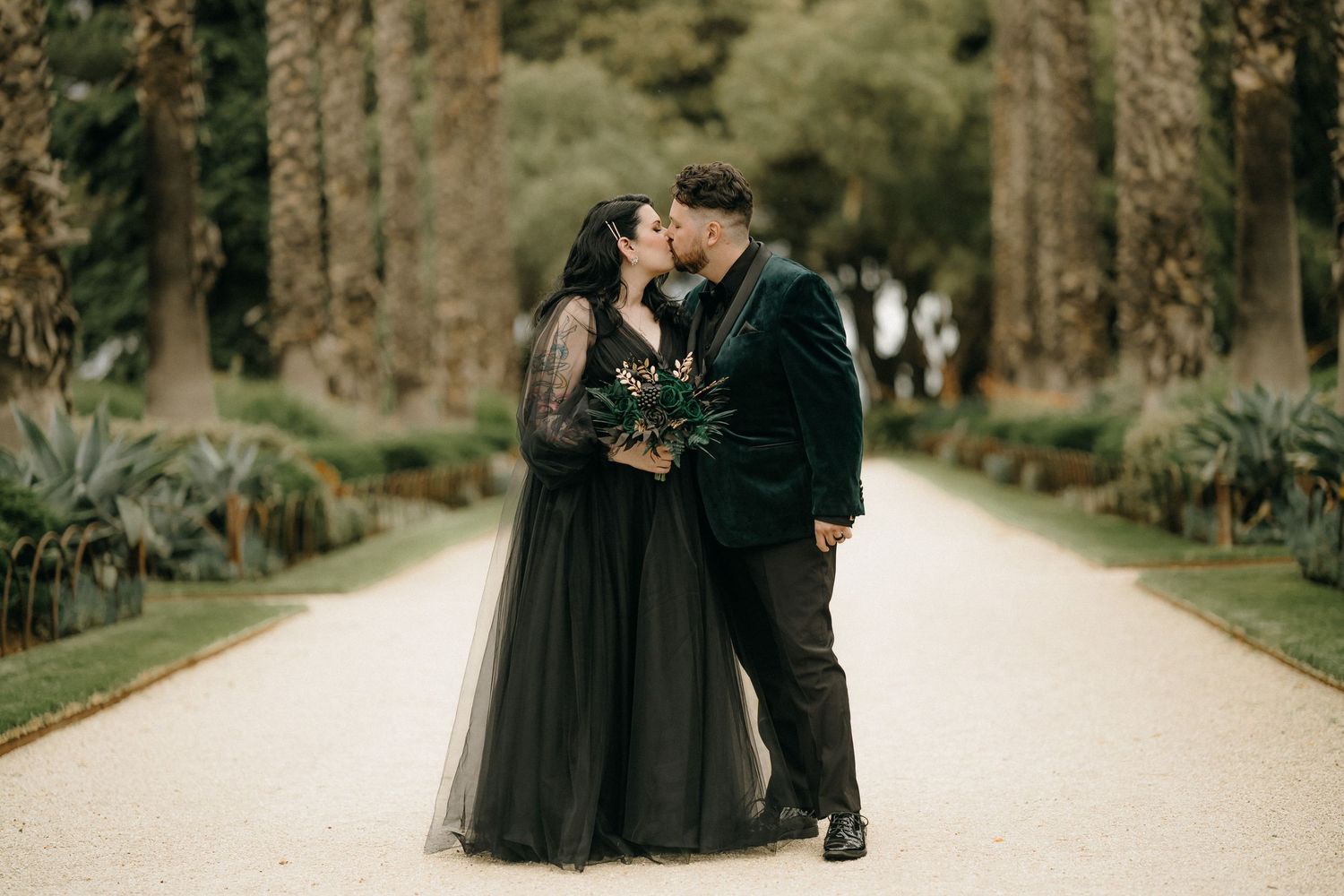 A couple in formal attire embraces on a tree-lined pathway during a romantic outdoor photo session.