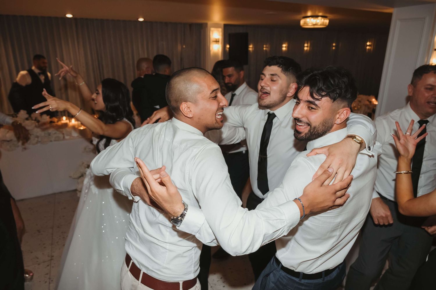 The newlyweds perform their first dance as guests watch from the edges of a softly lit ballroom dance floor.