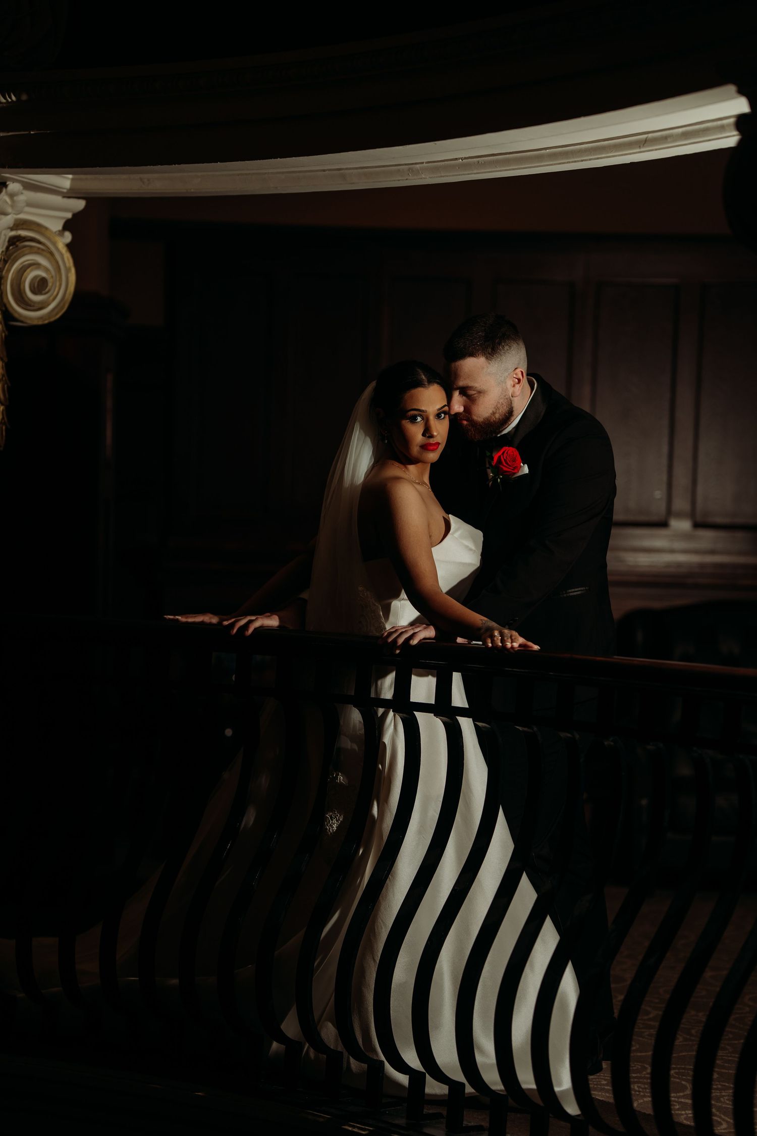 Bride in black and white striped gown with groom in dark suit sharing romantic moment on dimly lit balcony.