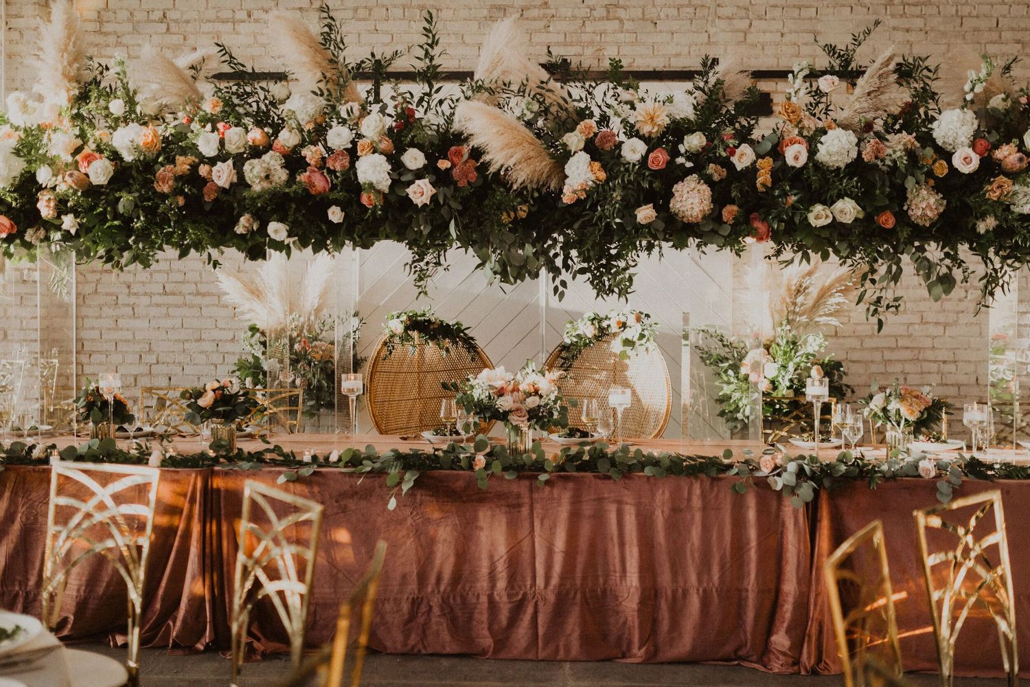 Elegant wedding reception venue with rustic wooden tables and chairs decorated with lush floral garlands and warm lighting.