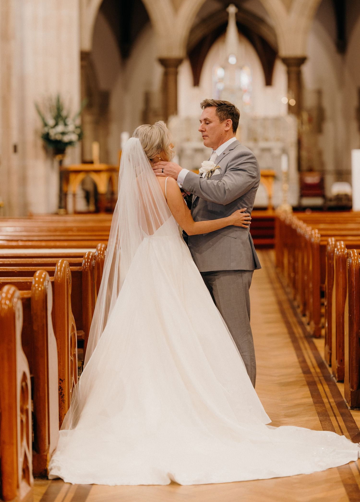 A couple shares a tender moment in the aisle of a beautiful church with gothic arches and wooden pews.