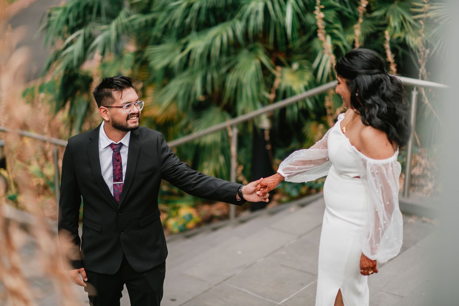 Romantic wedding couple shares intimate moments in a lush tropical garden setting with palm trees in the background.
