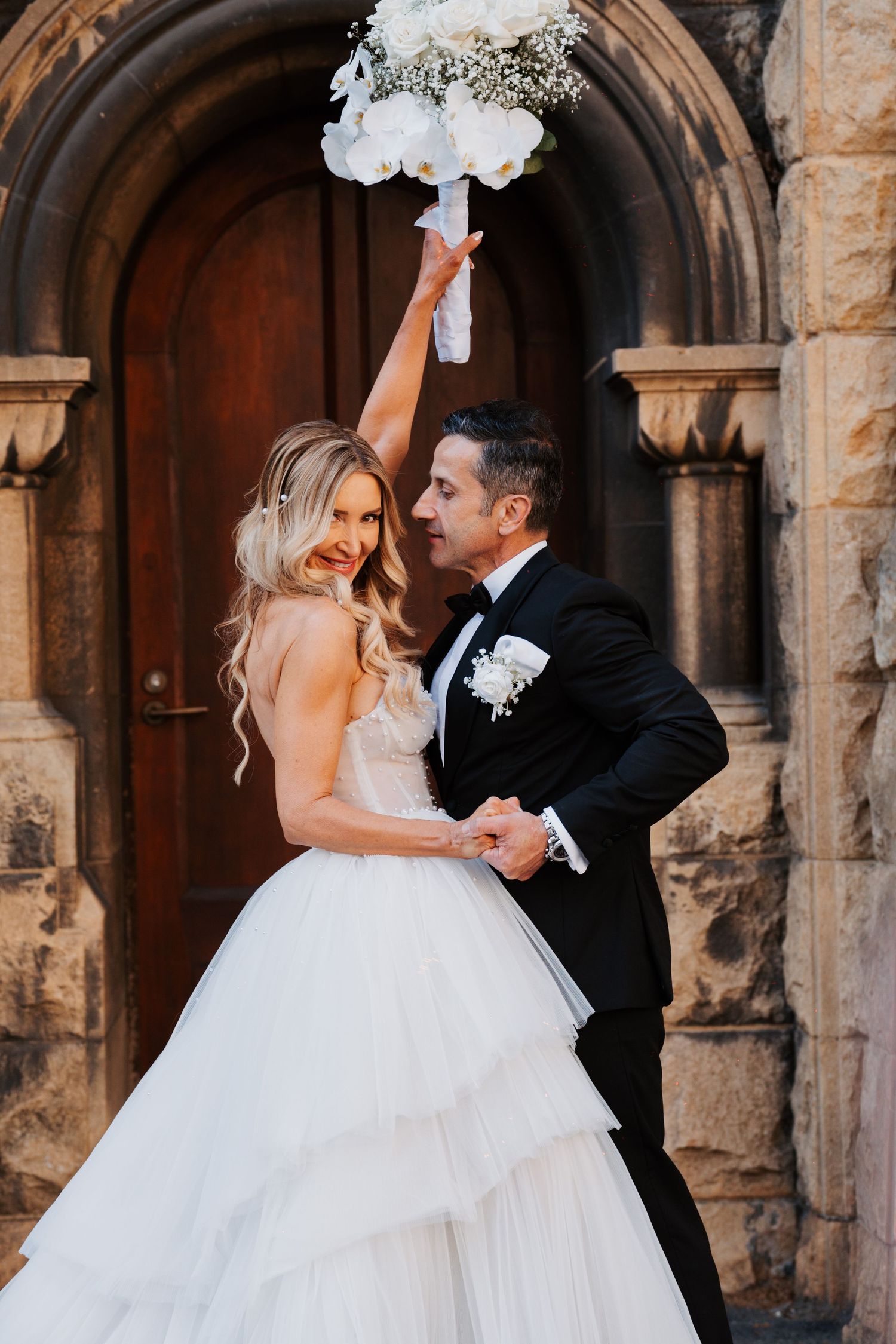 Romantic wedding couple shares an intimate moment in front of a historic stone archway with elegant architectural details.