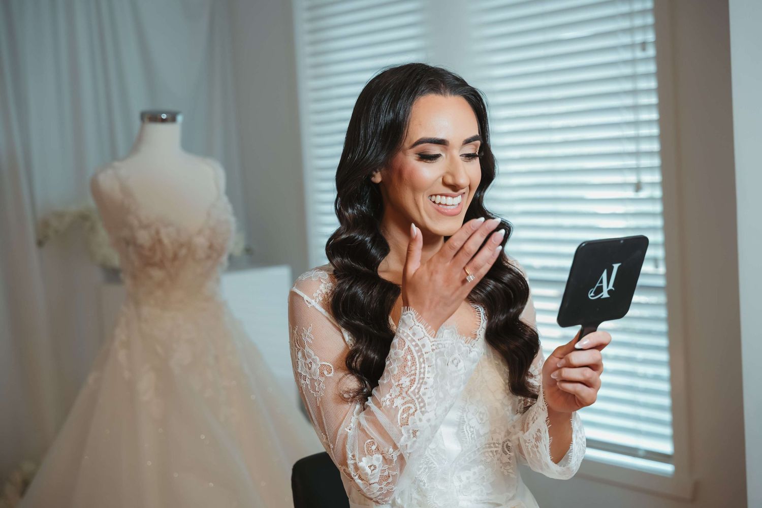 Bride in lace sleeve dress reads card with emotional reaction while dress form with gown stands in background.