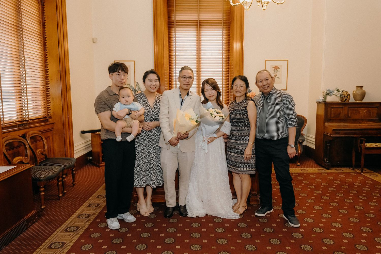 Family group poses together in a vintage-style interior room with ornate carpet and wooden furniture.
