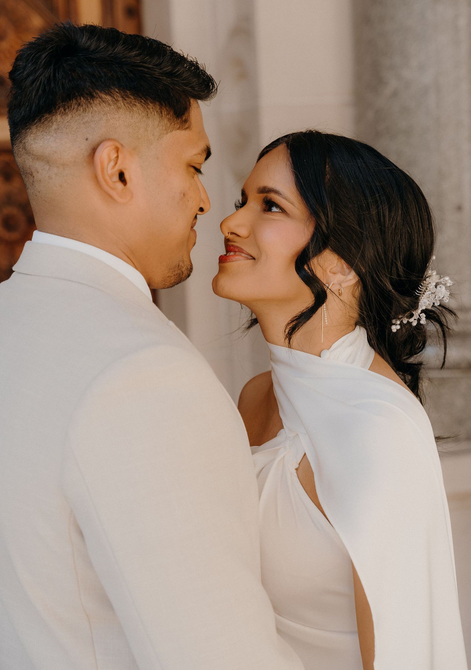 A romantic couple in white attire share an intimate moment during their wedding photoshoot.