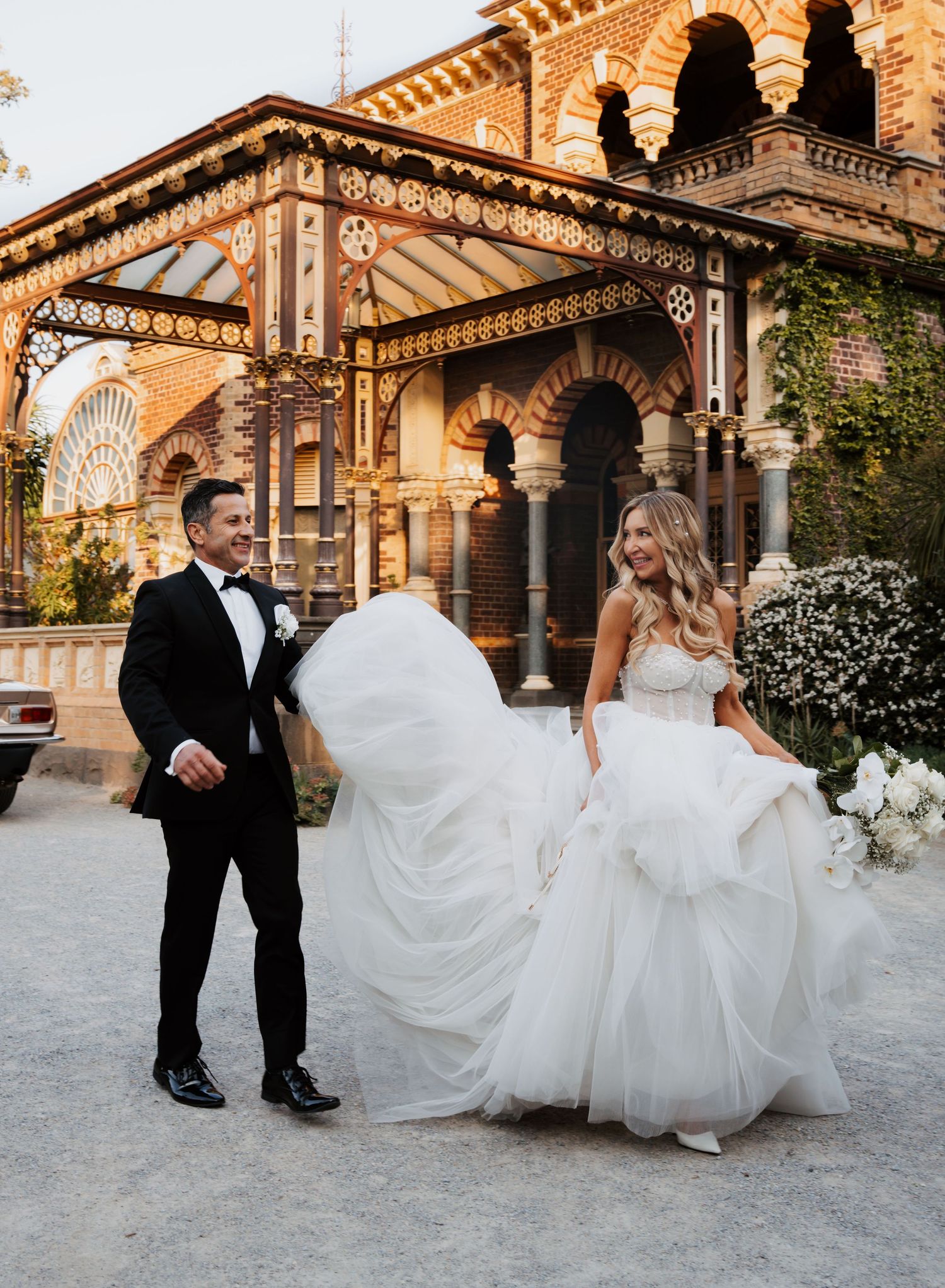 A couple in wedding attire dances and twirls on a stone patio in front of an ornate Moorish-style architectural backdrop.