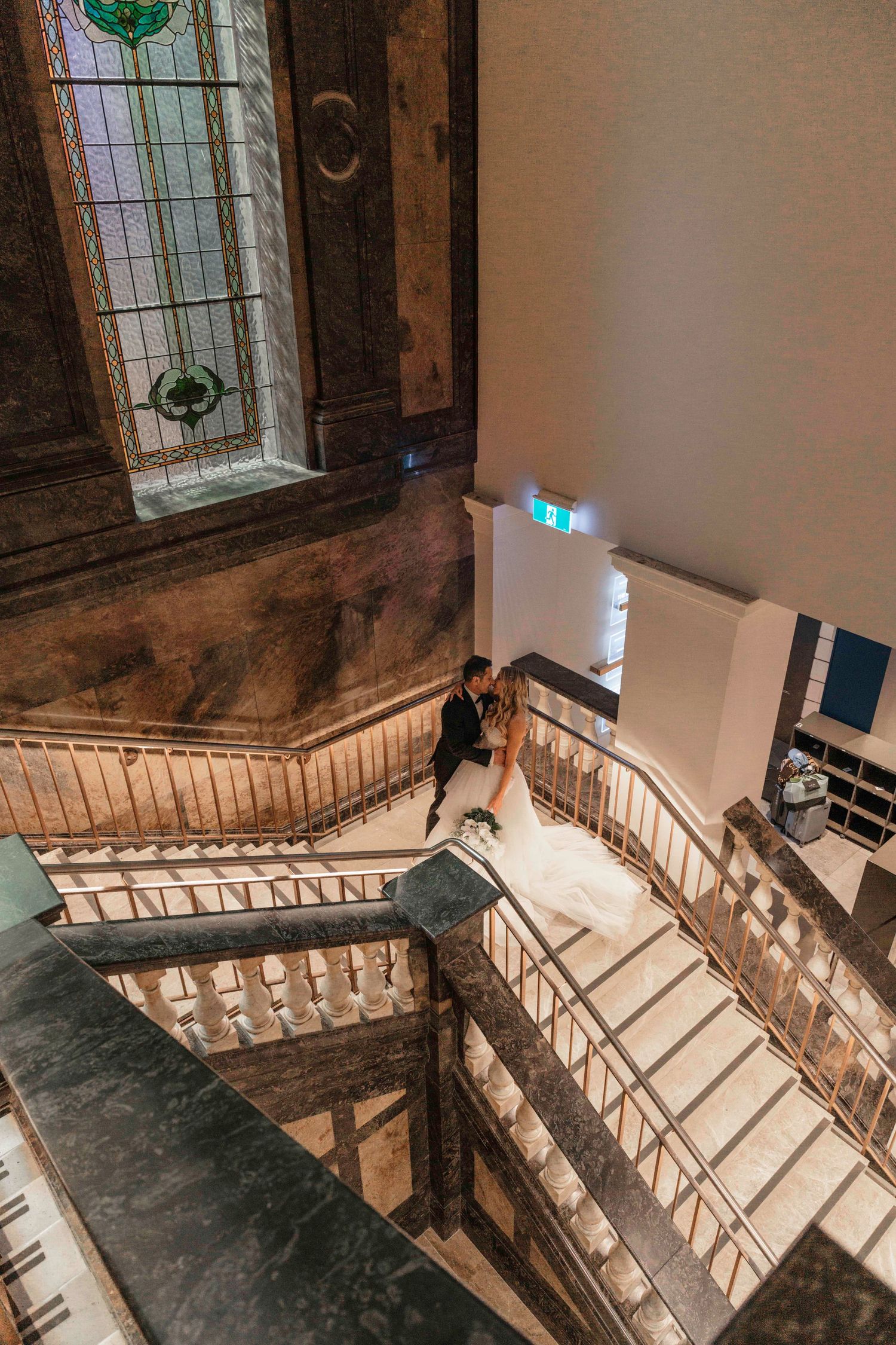 Historic wooden spiral staircase with ornate balustrade winds upward in an old building with stained glass windows.