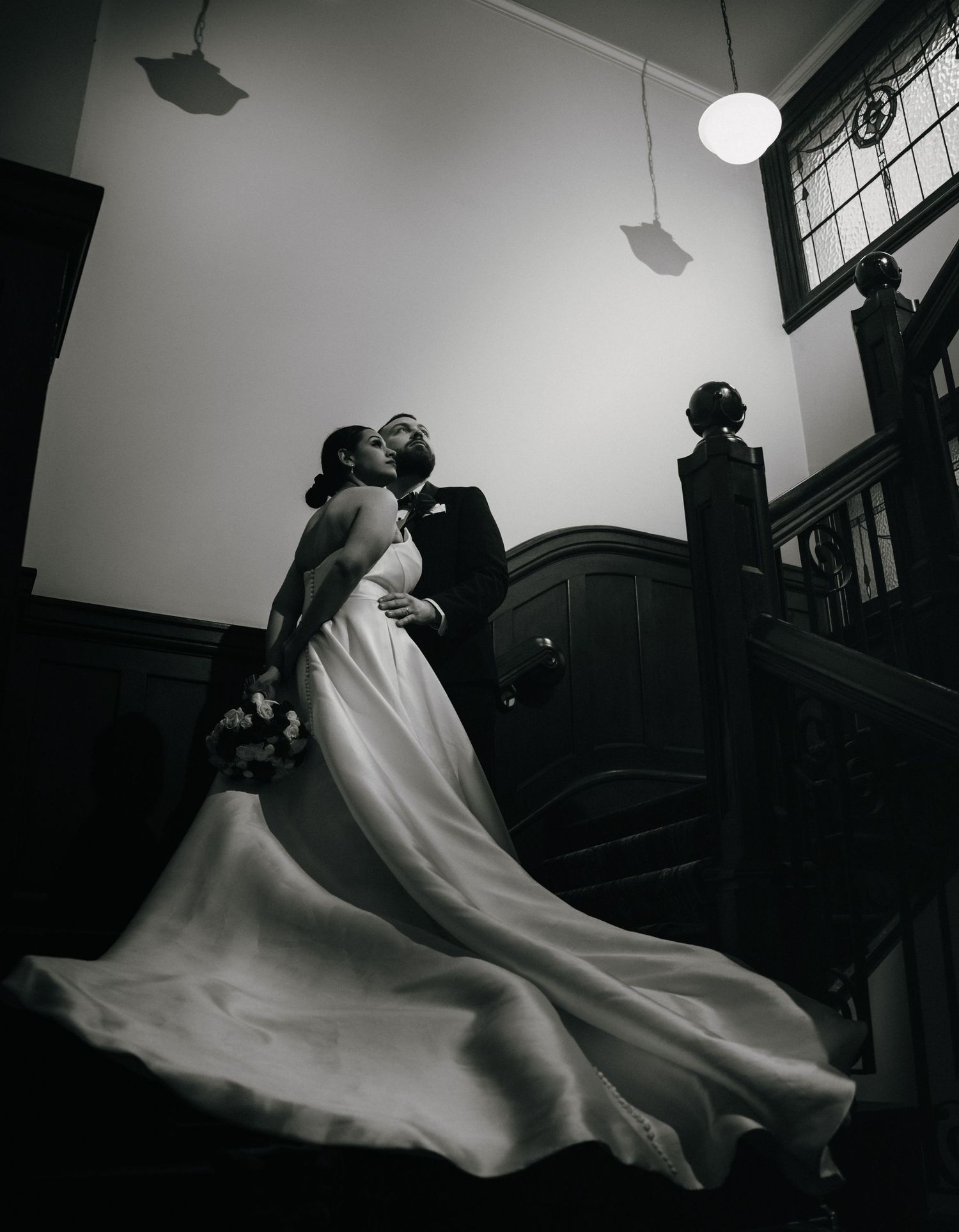 Black and white wedding photo of bride and groom kissing on grand staircase, brides train flowing dramatically.