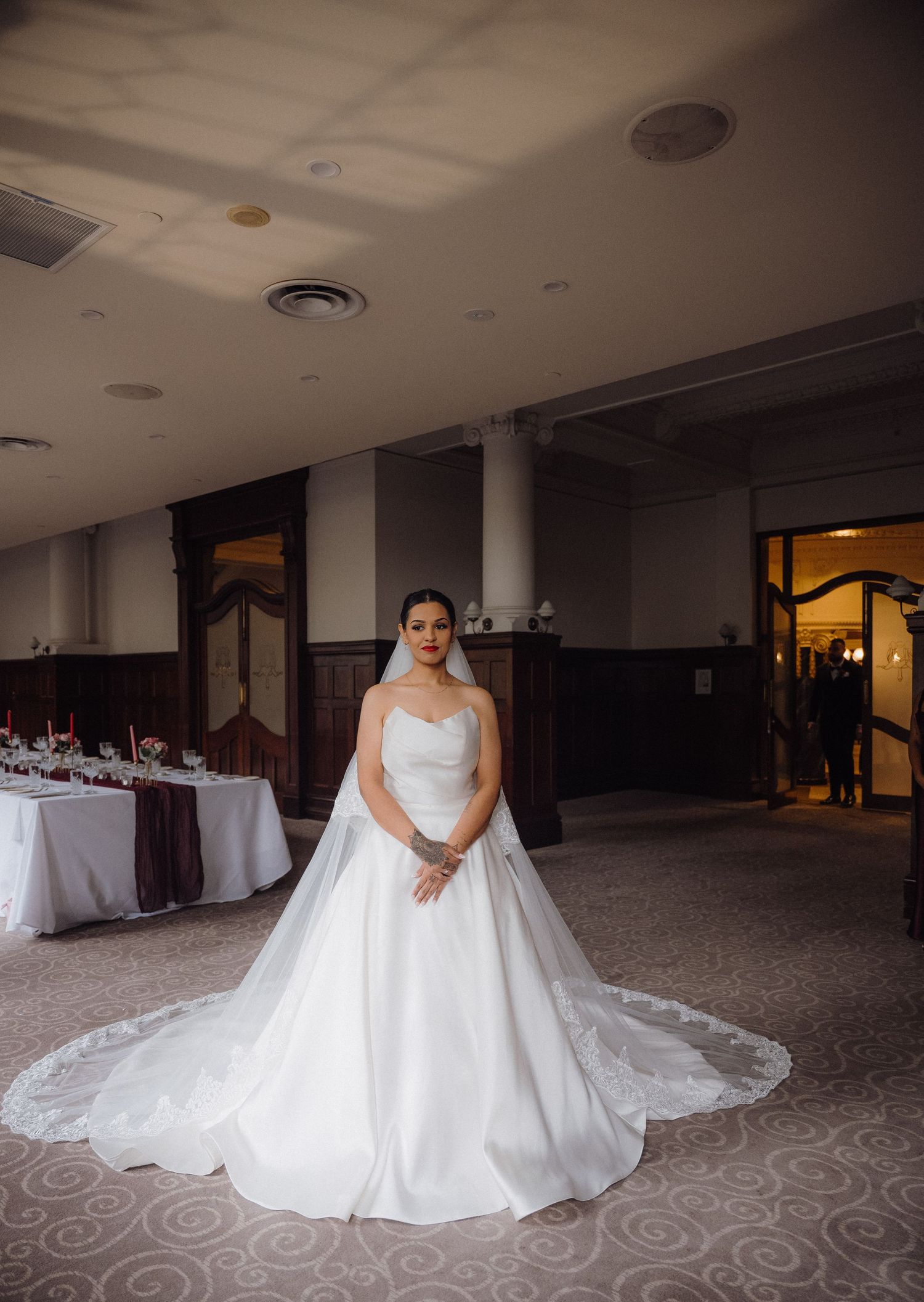 Bride in a strapless white ballgown wedding dress standing in an elegant reception hall with draped tables.