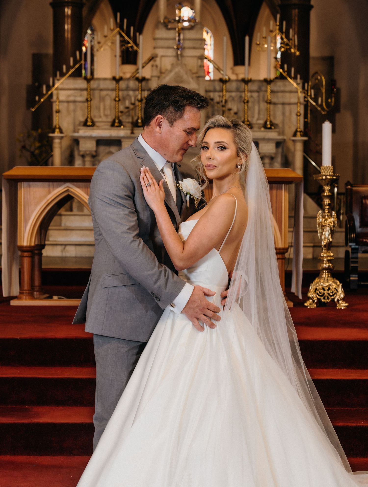 A romantic wedding portrait of a couple embracing at the altar in a grand cathedral with ornate gold details.
